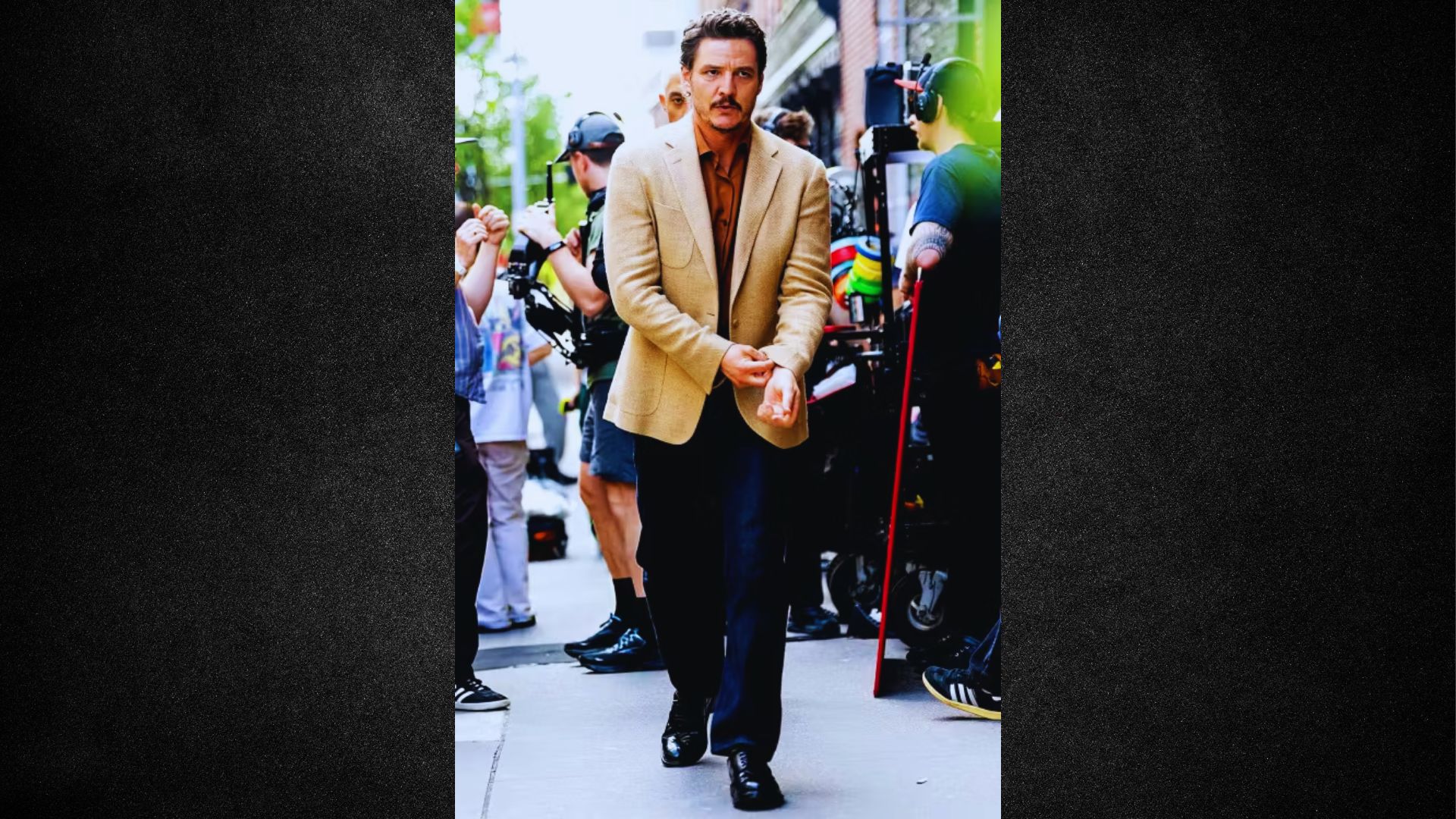A man dressed in a tan suit strolling along the sidewalk, with buildings visible in the background.