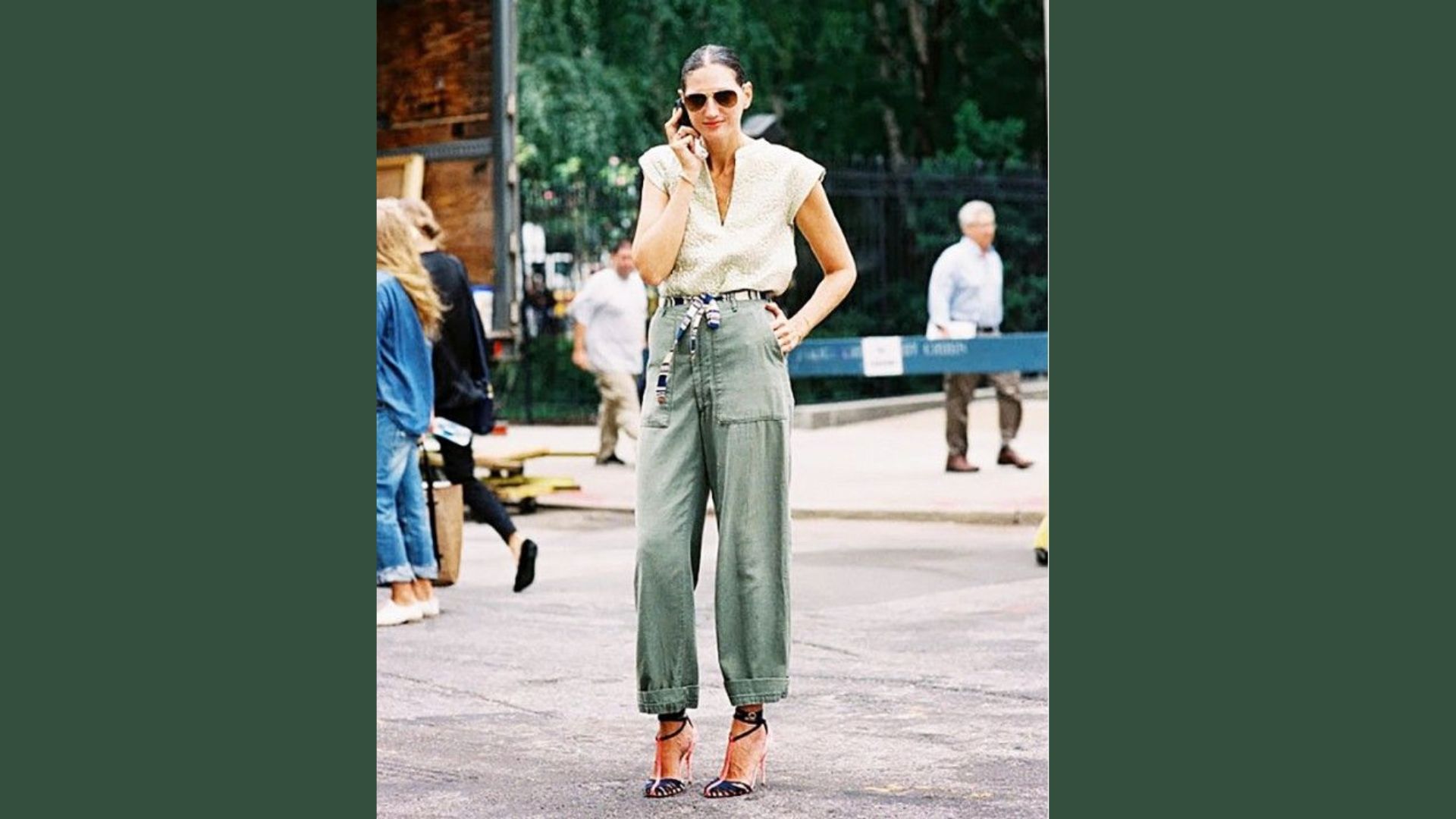 A woman wearing green pants and a white shirt stands confidently, showcasing a casual yet stylish outfit.