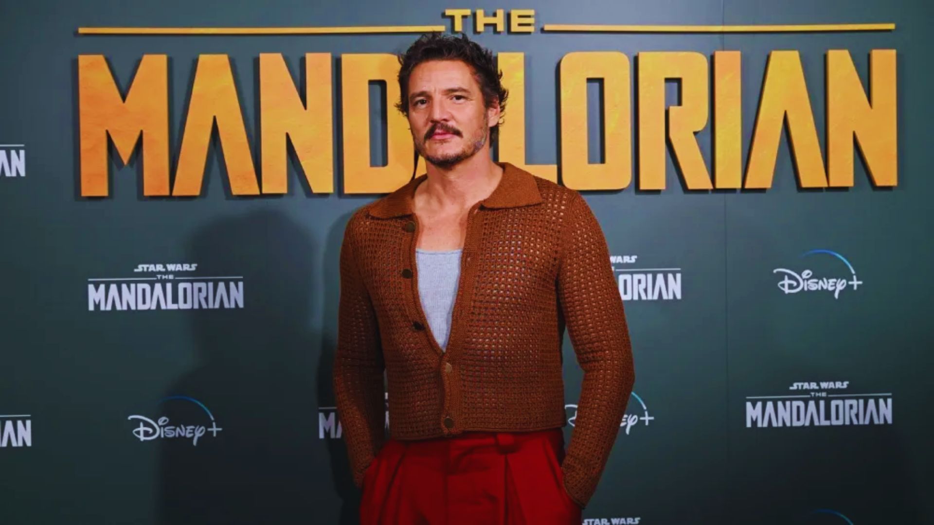 The Mandalorian actor poses for a photo at the premiere, smiling and dressed in formal attire against a red carpet backdrop.