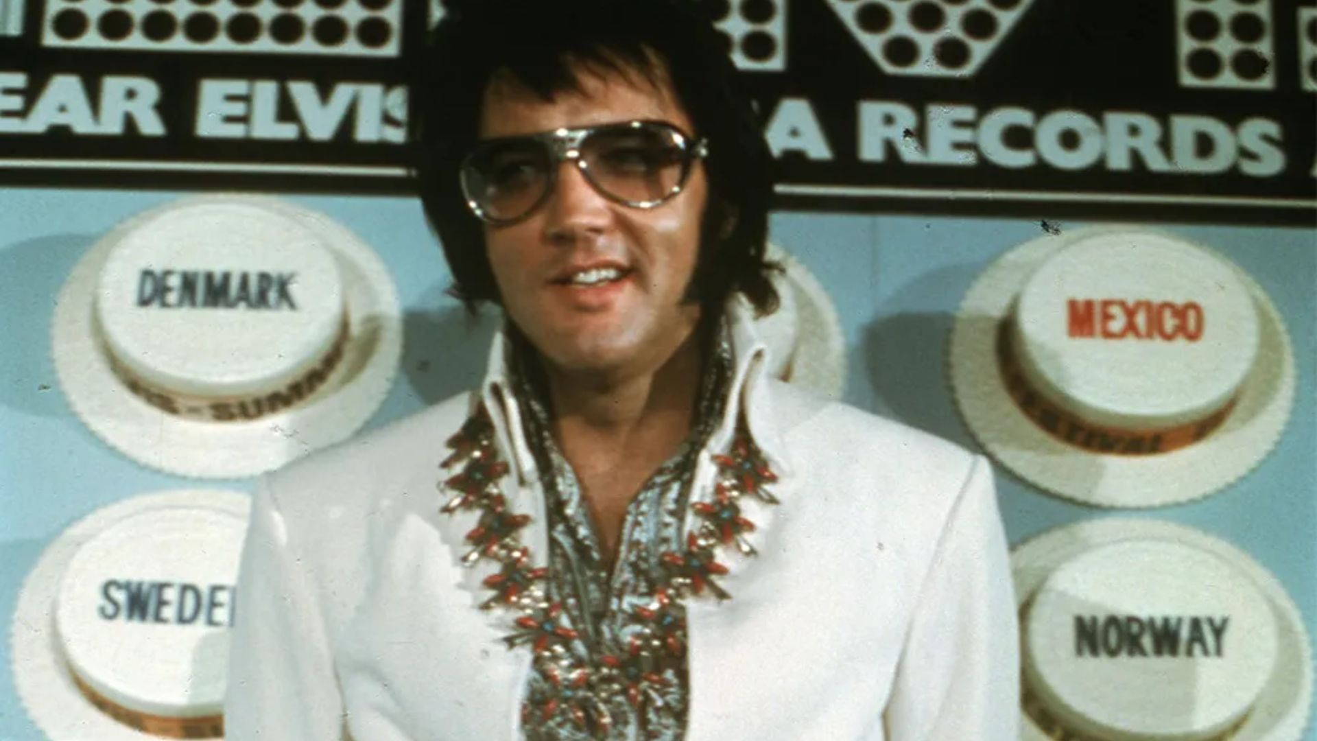 Elvis Presley performing on stage in the 1970s, wearing a flashy jumpsuit and exuding charisma.