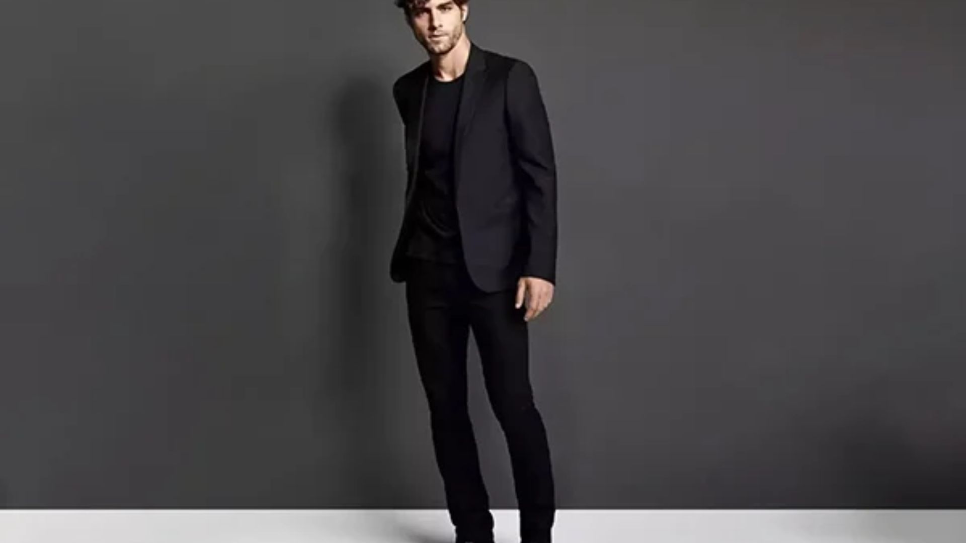 A man dressed in a black suit and black shoes, showcasing a stylish party outfit for a Saltburn event
