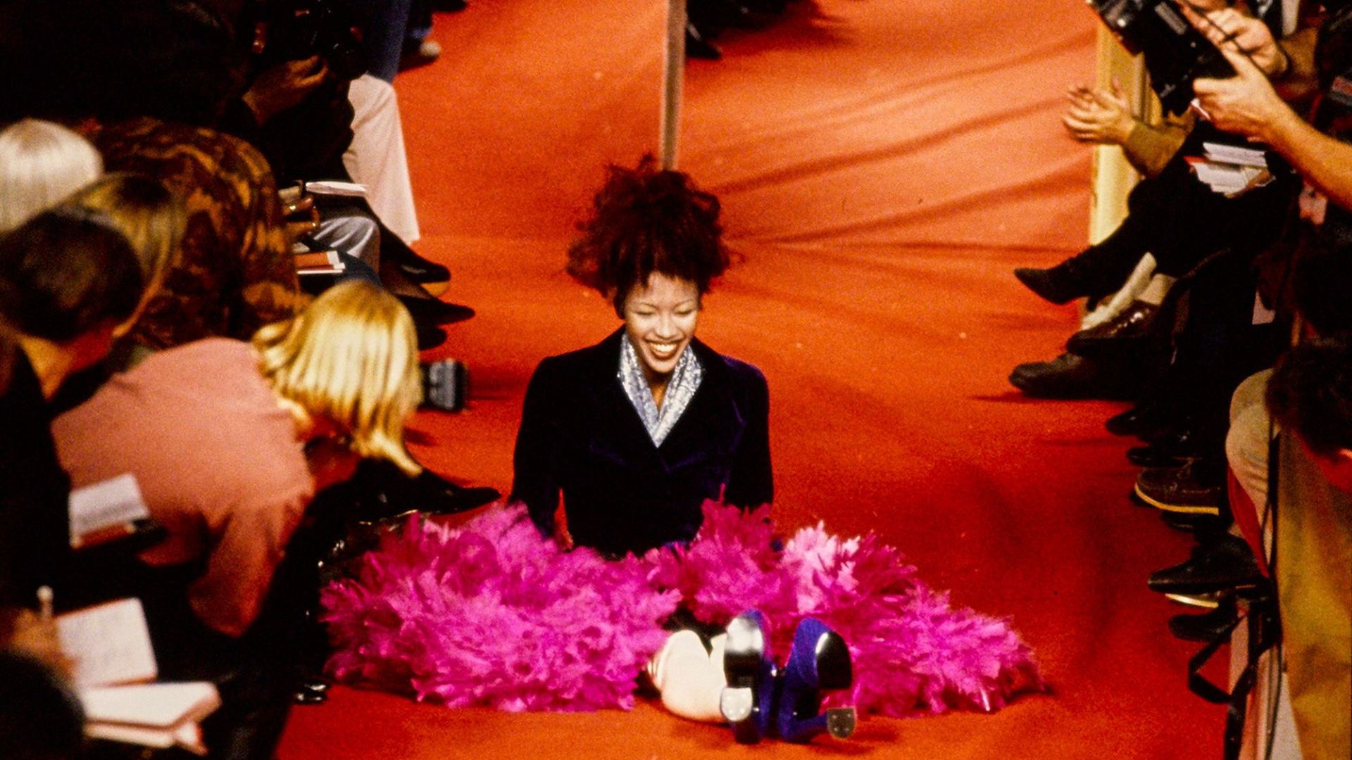 Naomi Campbell seated on the runway, holding a pink feather, from Vivienne Westwood's Fall 1993 Paris Runway Show.