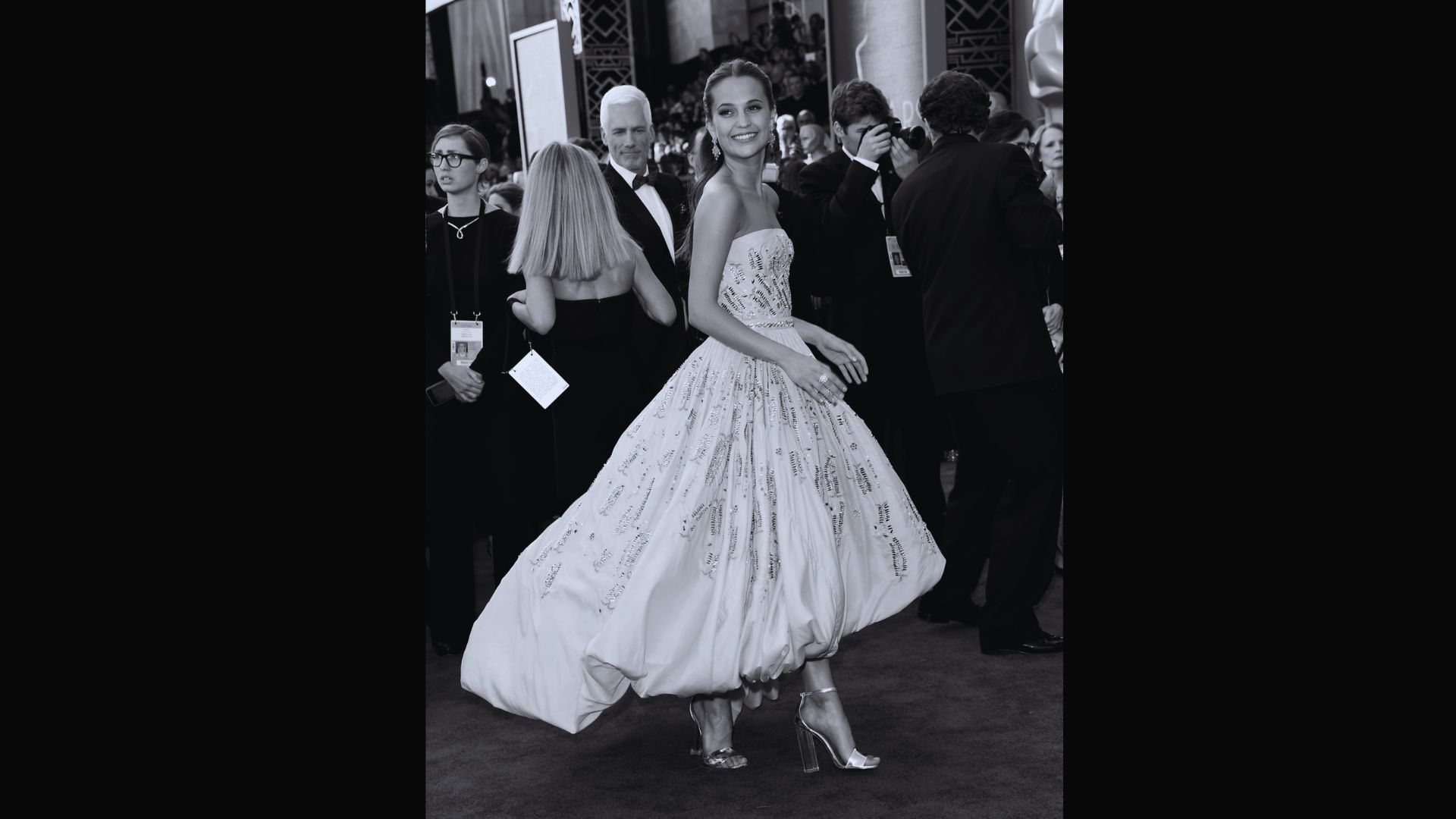 A woman in a flowing white dress gracefully walks down a vibrant red carpet.