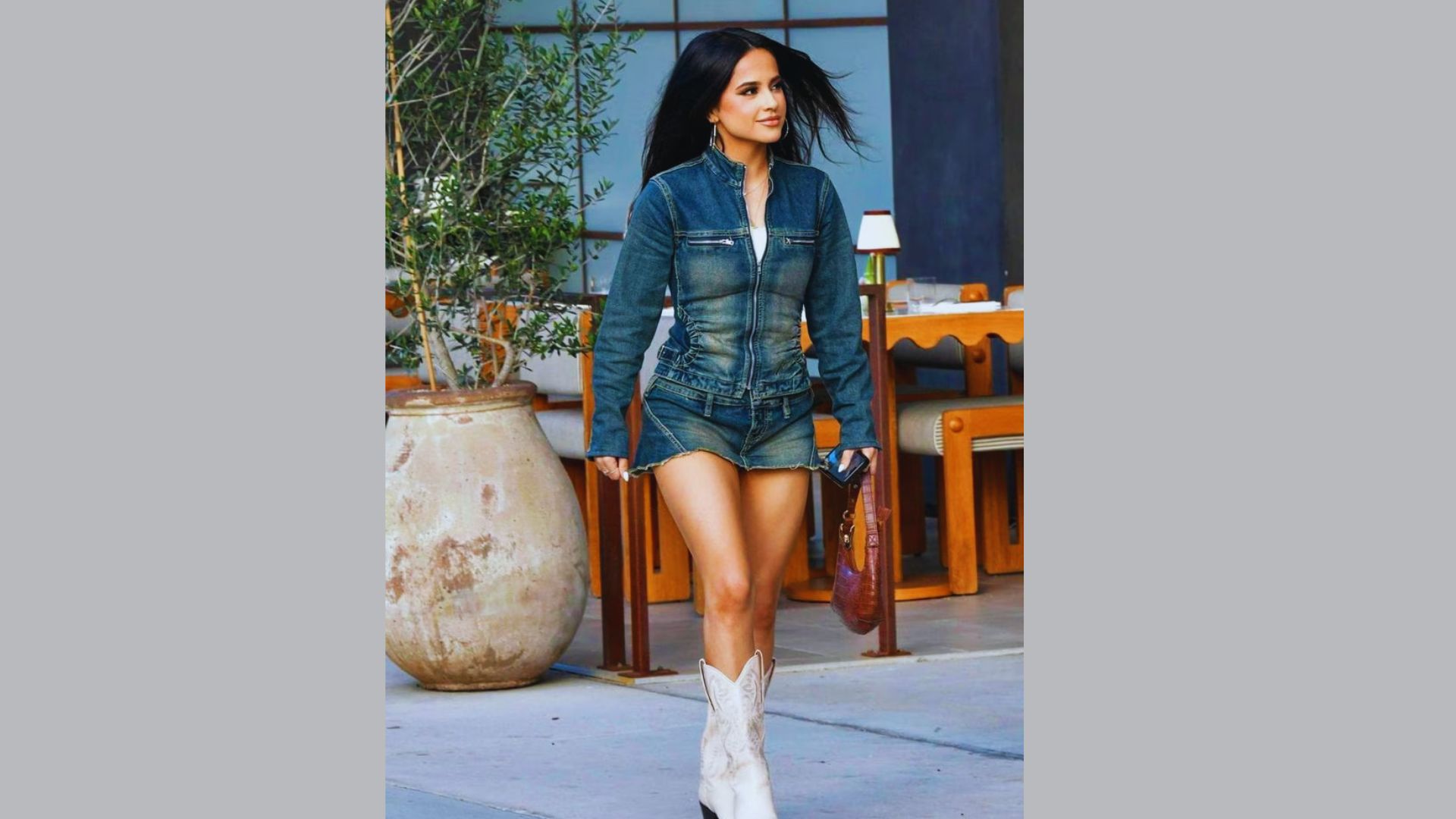 Person wearing a denim romper and cowboy boots, standing confidently in a casual outdoor setting.