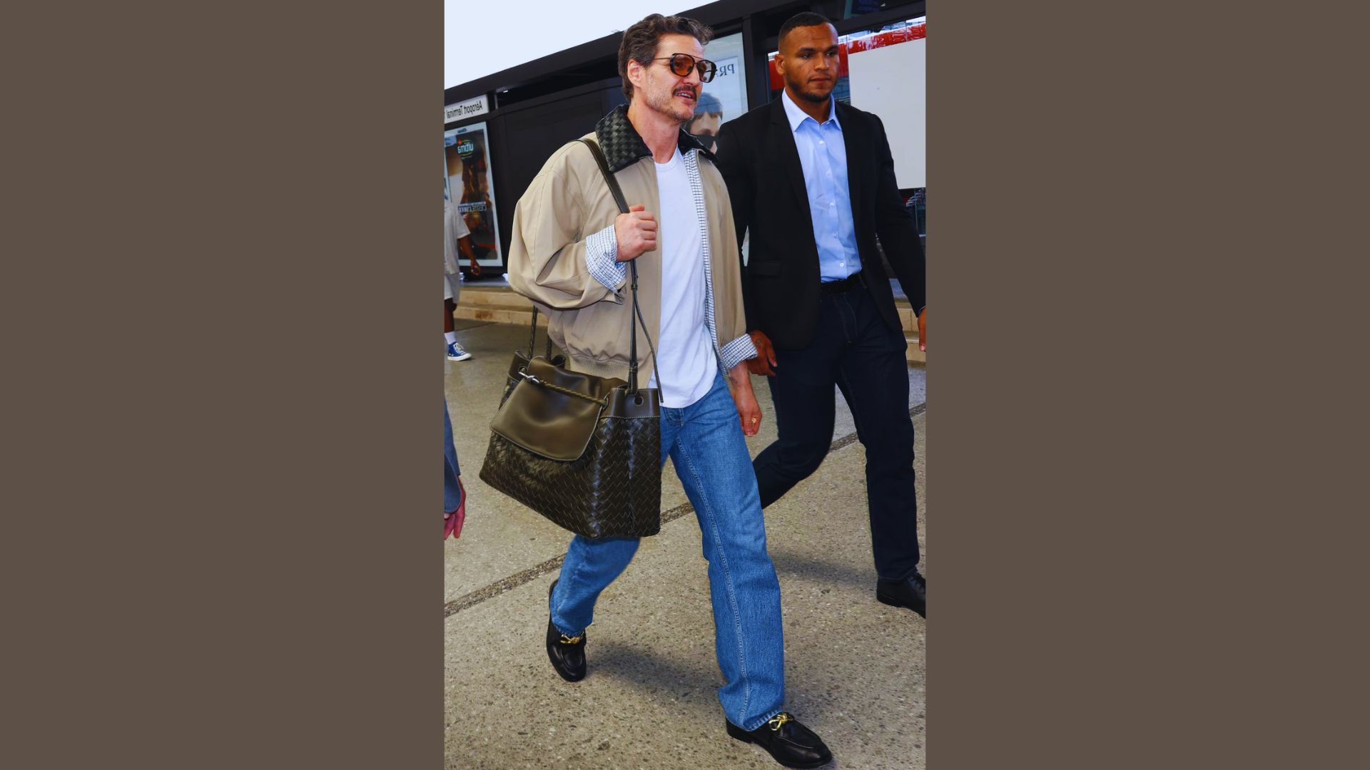 A man wearing jeans and a white shirt carries a bag, walking confidently down a city street.