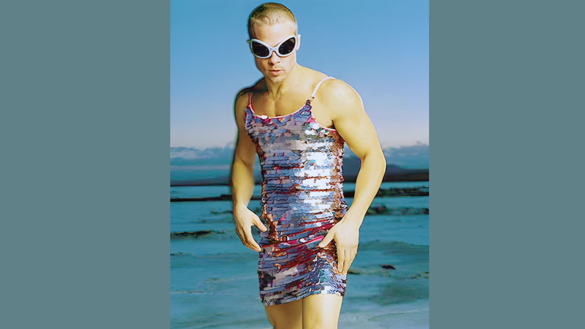 Brad Pitt, wearing a dress and sunglasses, stands confidently on a sunny beach.