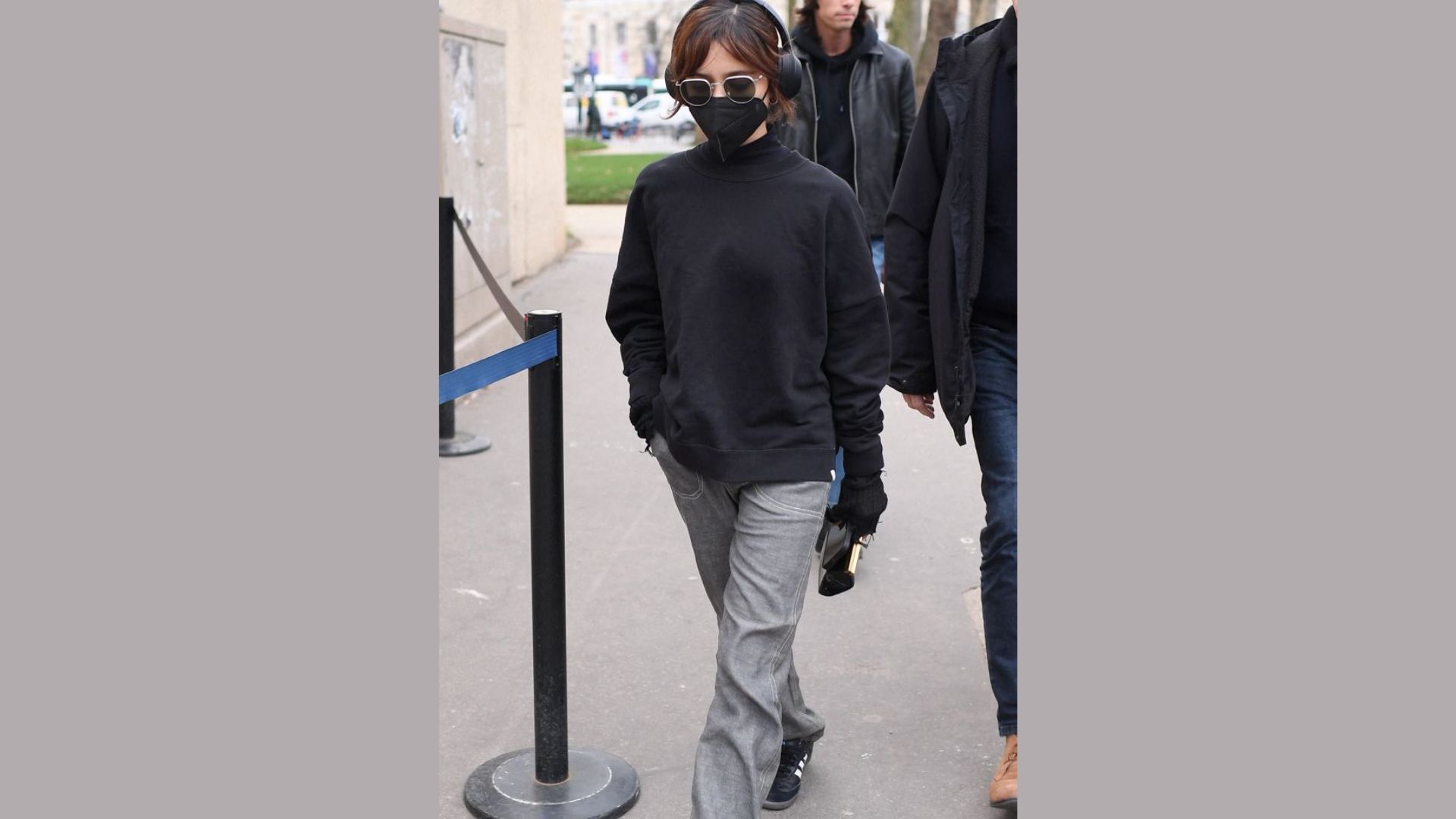 A woman in an oversized black hoodie and tailored grey pants stands confidently, showcasing a casual yet stylish outfit.