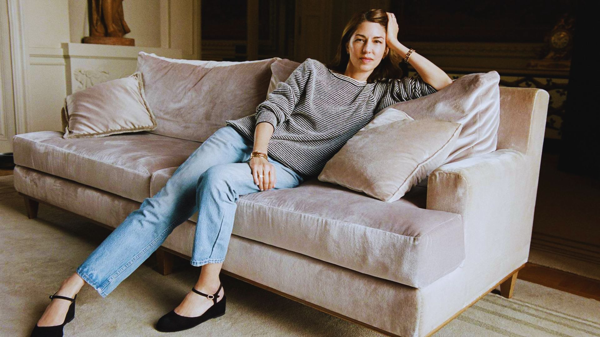 A woman sitting comfortably on a couch in a cozy room, surrounded by soft lighting and decorative elements.