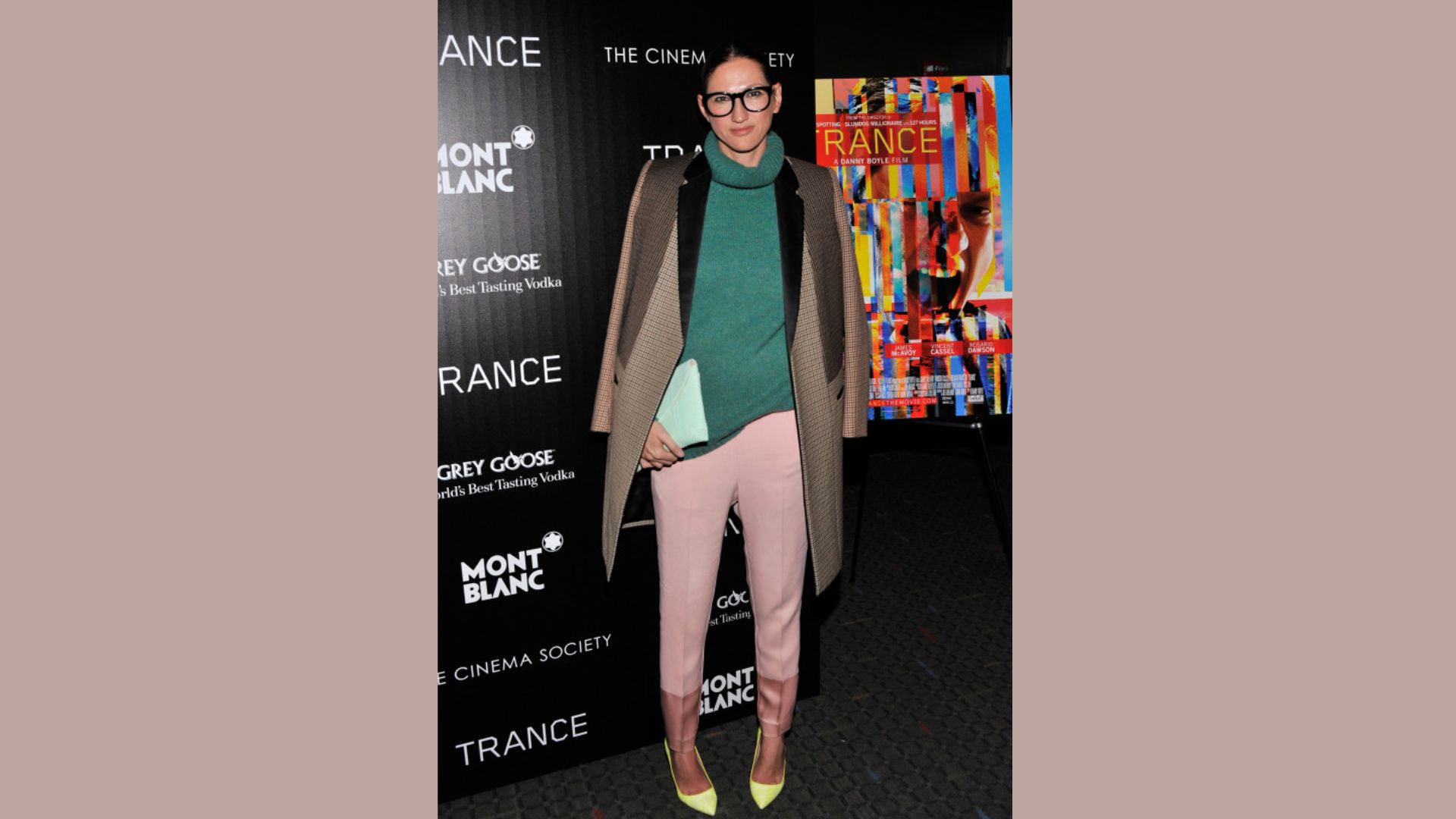 A woman in a green sweater and pink pants smiles, displaying her colorful and trendy attire.