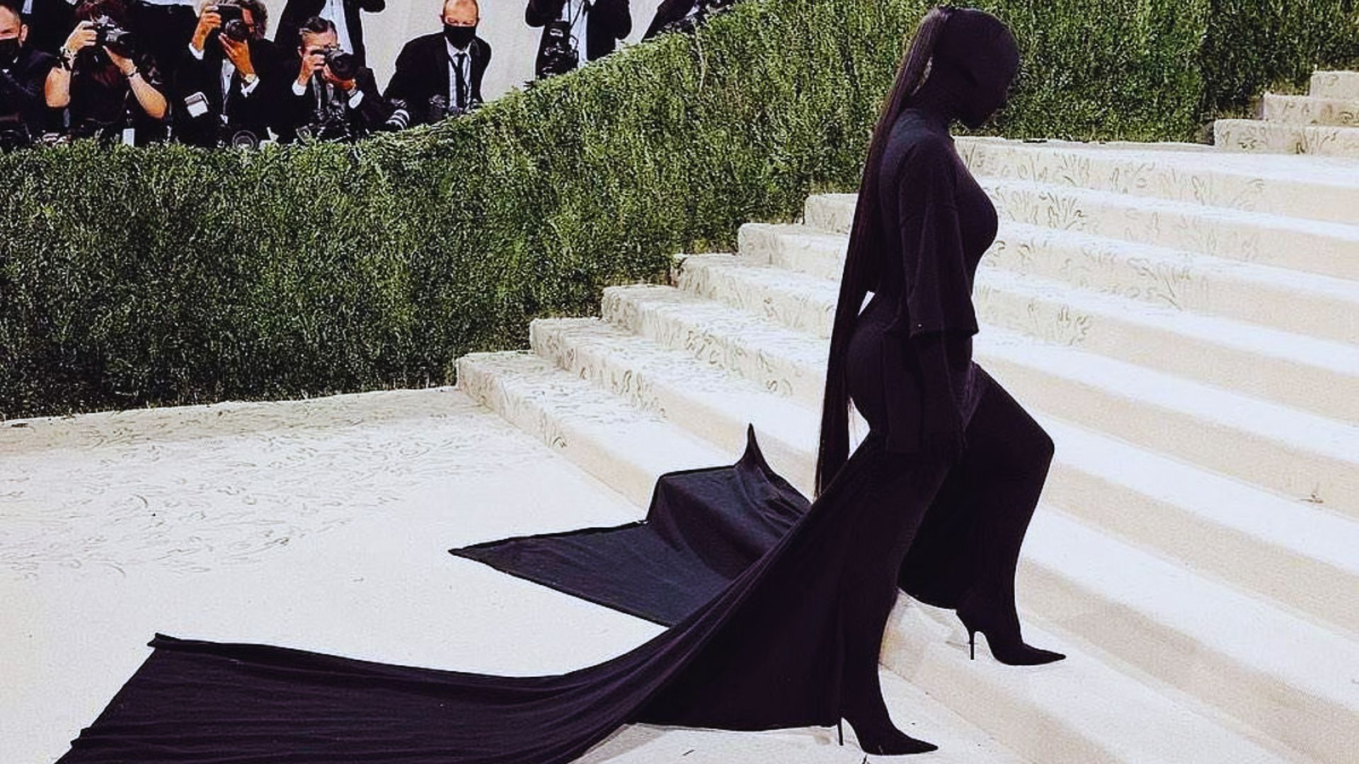 A woman in a black dress and cape gracefully descends a staircase.