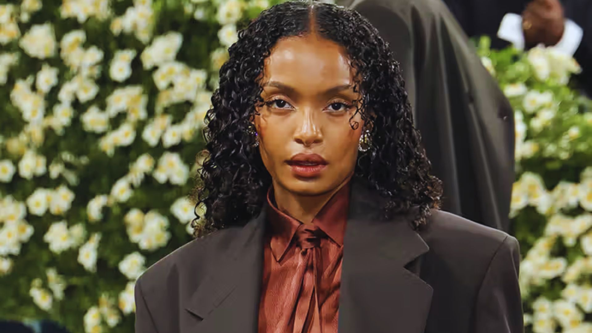 A woman with curly hair dressed in a professional suit, exuding confidence and style.