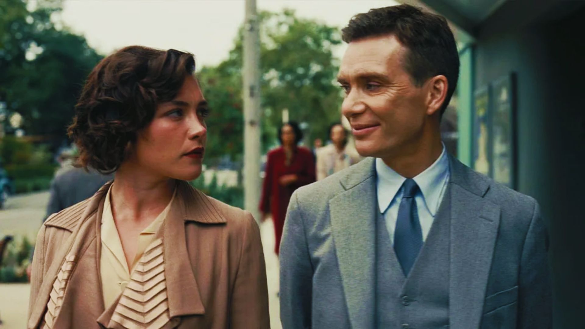 A man and woman stand side by side, both dressed in period attire, in a scene inspired by Oppenheimer.