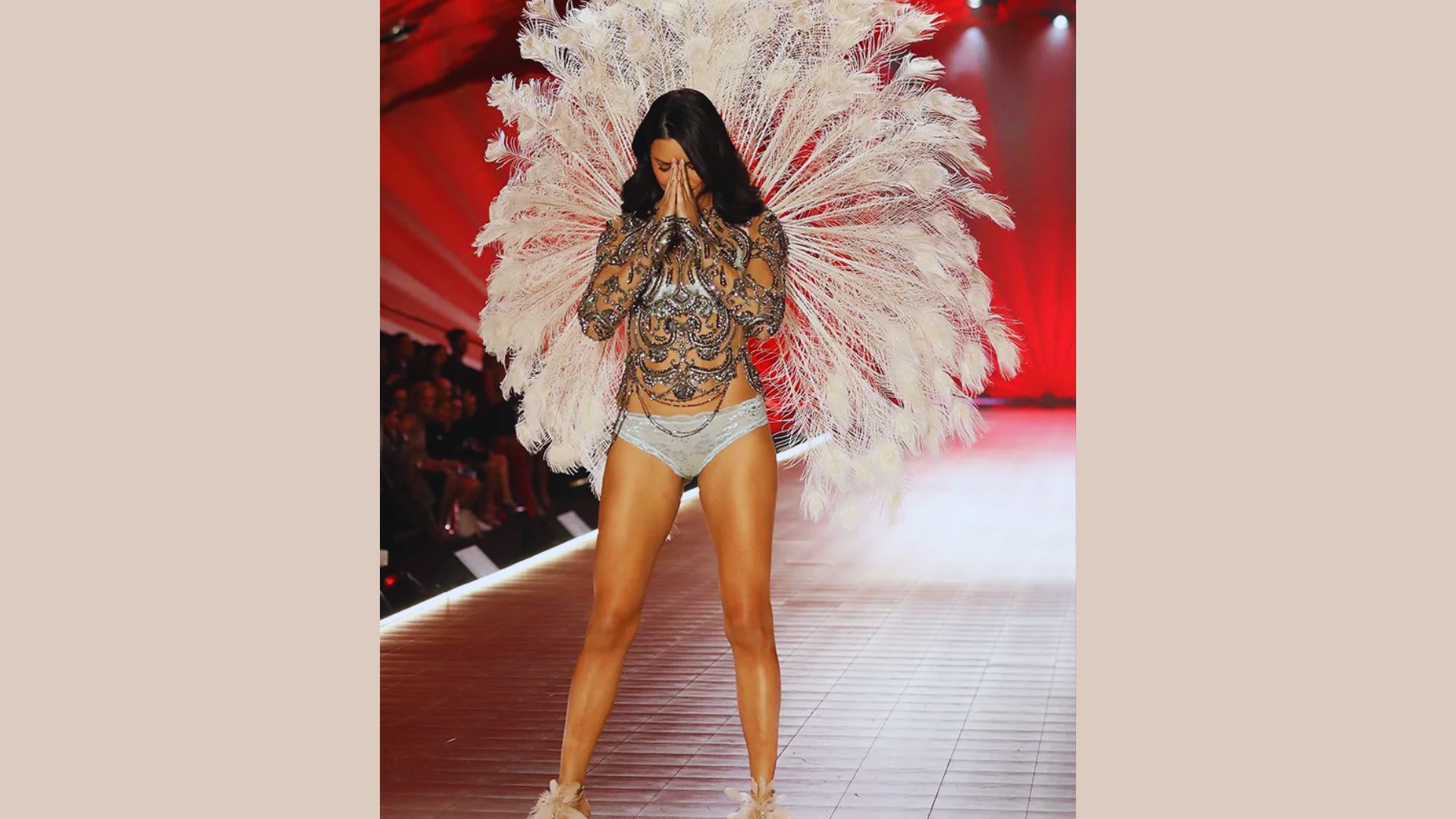 A woman in a white feather costume confidently walks down a runway, showcasing her outfit to the audience.