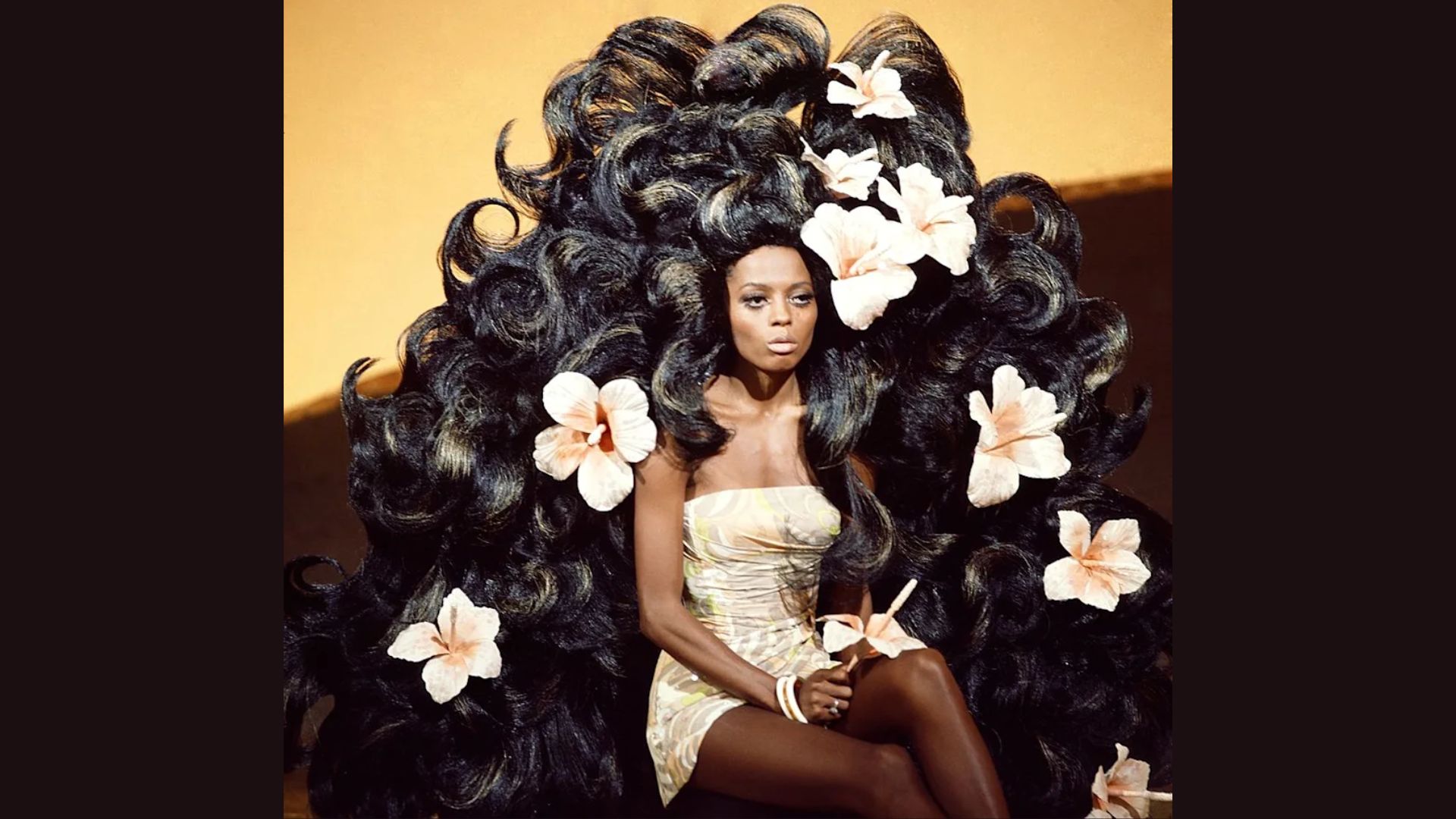 1. A woman with long hair sits on a chair surrounded by colorful flowers, creating a serene and inviting atmosphere.