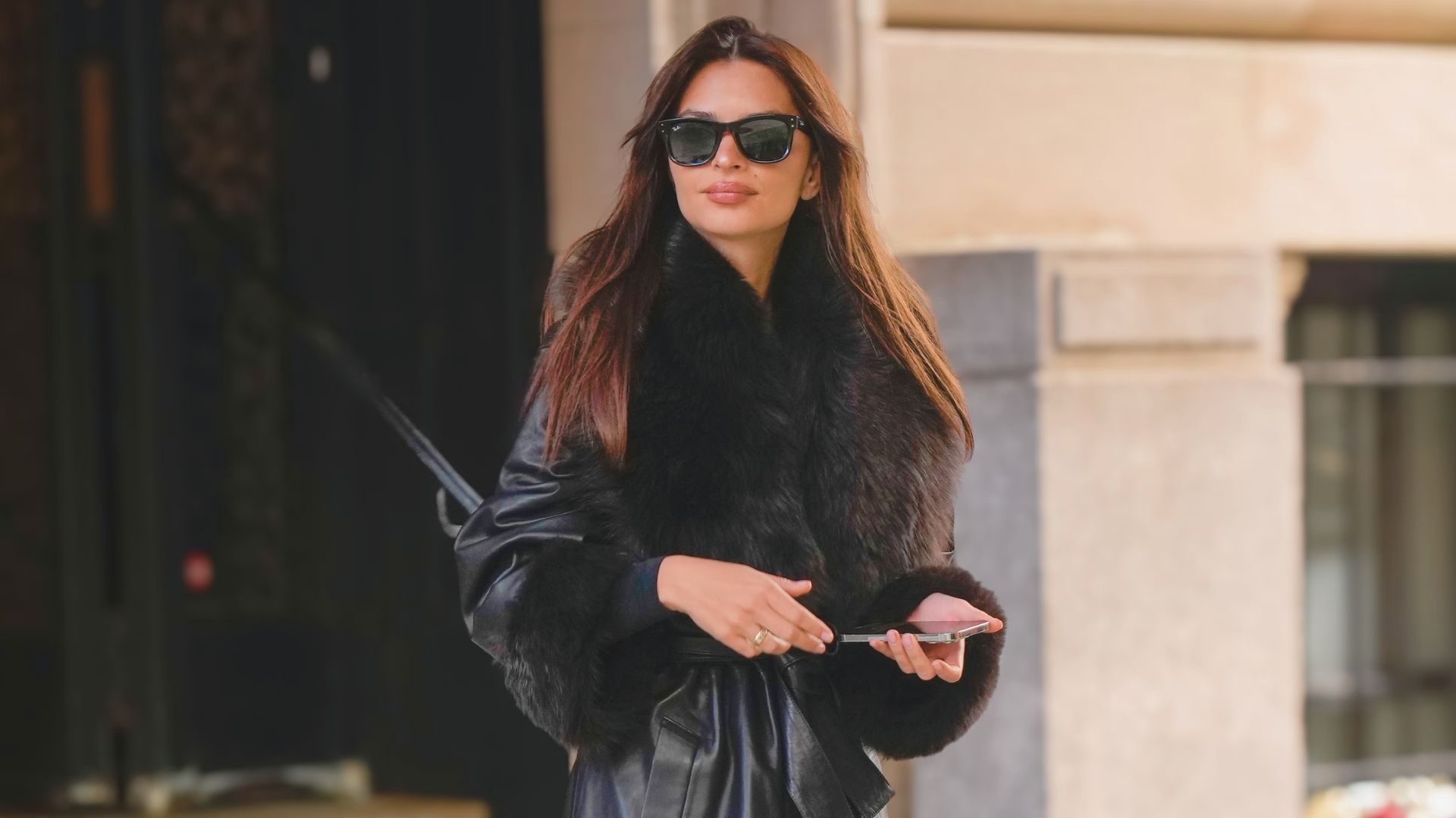 A woman wearing a black leather jacket and sunglasses stands confidently, exuding a cool and stylish vibe.