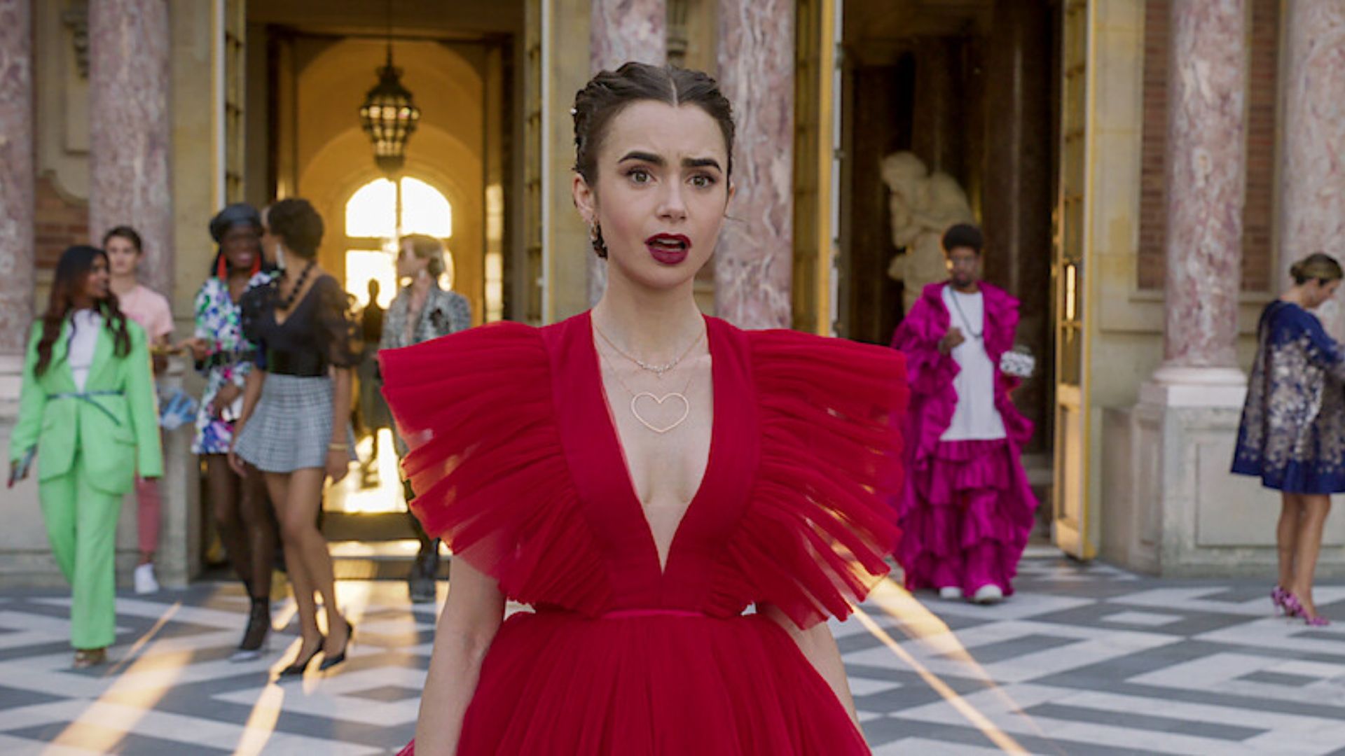 A woman in a red dress stands confidently in front of a building, showcasing her stylish outfit against the urban backdrop.