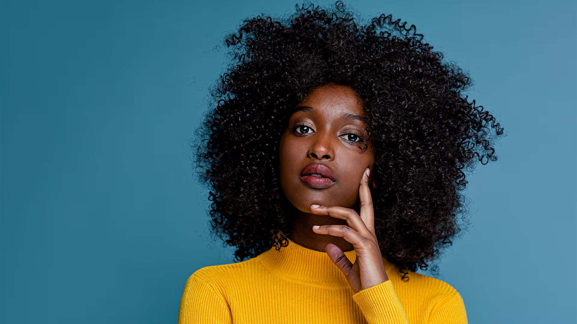 A woman with curly hair wearing a yellow sweater, showcasing Black Panther Party outfit inspiration and style ideas.