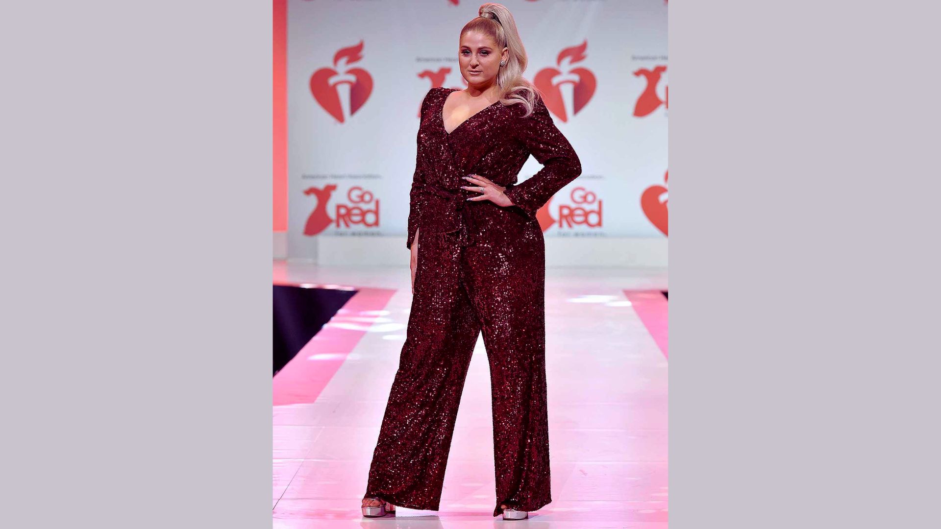 A woman walks the runway in a striking red sequin jumpsuit, showcasing a bold fashion statement.