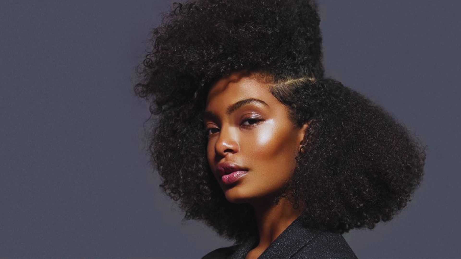 A woman with a voluminous afro hairstyle, showcasing natural curls and a confident expression.