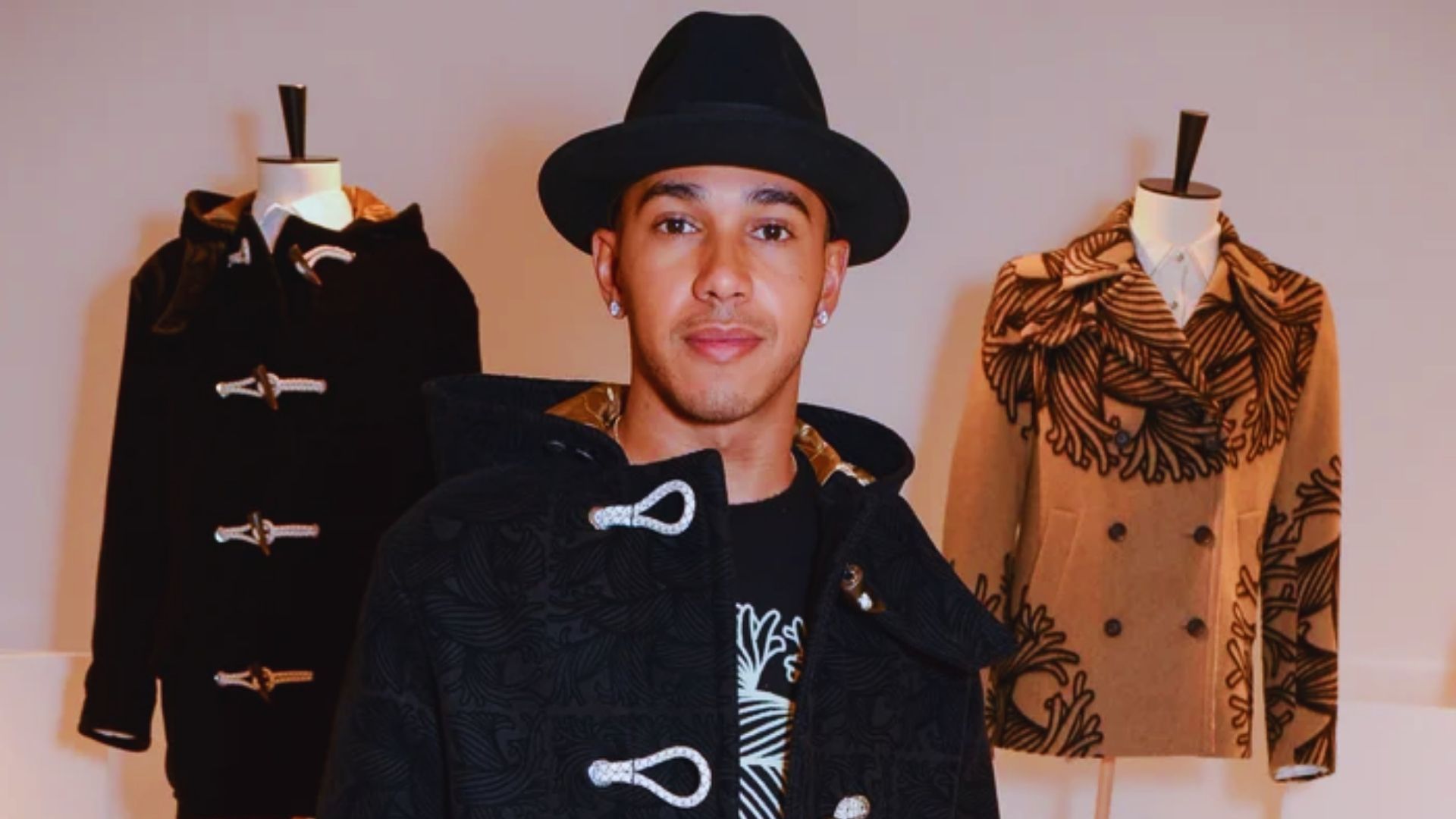 A man in a hat and jacket stands beside a display of various coats in a retail setting.