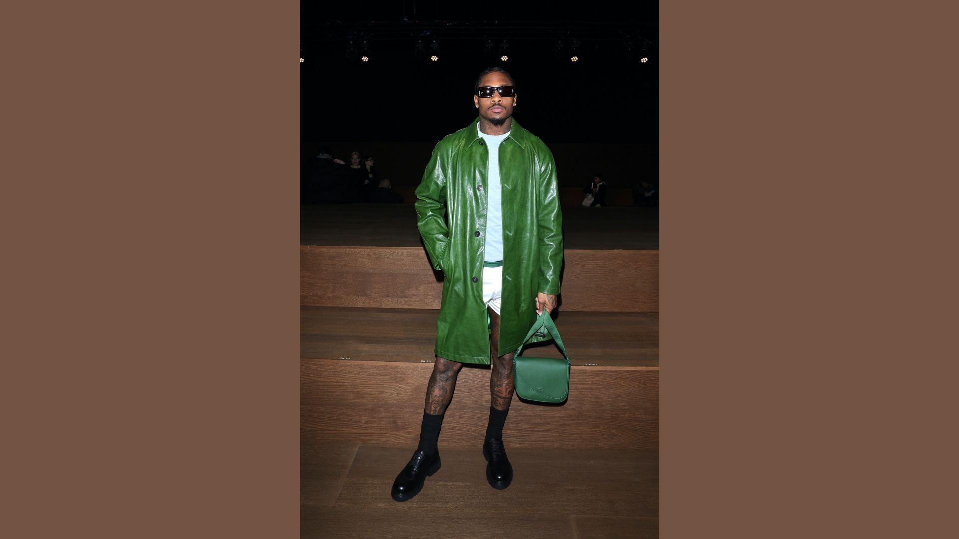A man wearing a green coat and white pants stands confidently, showcasing a stylish and casual outfit.