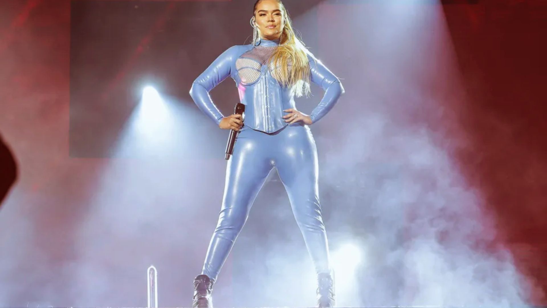 A woman wearing a blue latex outfit performs on stage, showcasing her dynamic presence and confidence.
