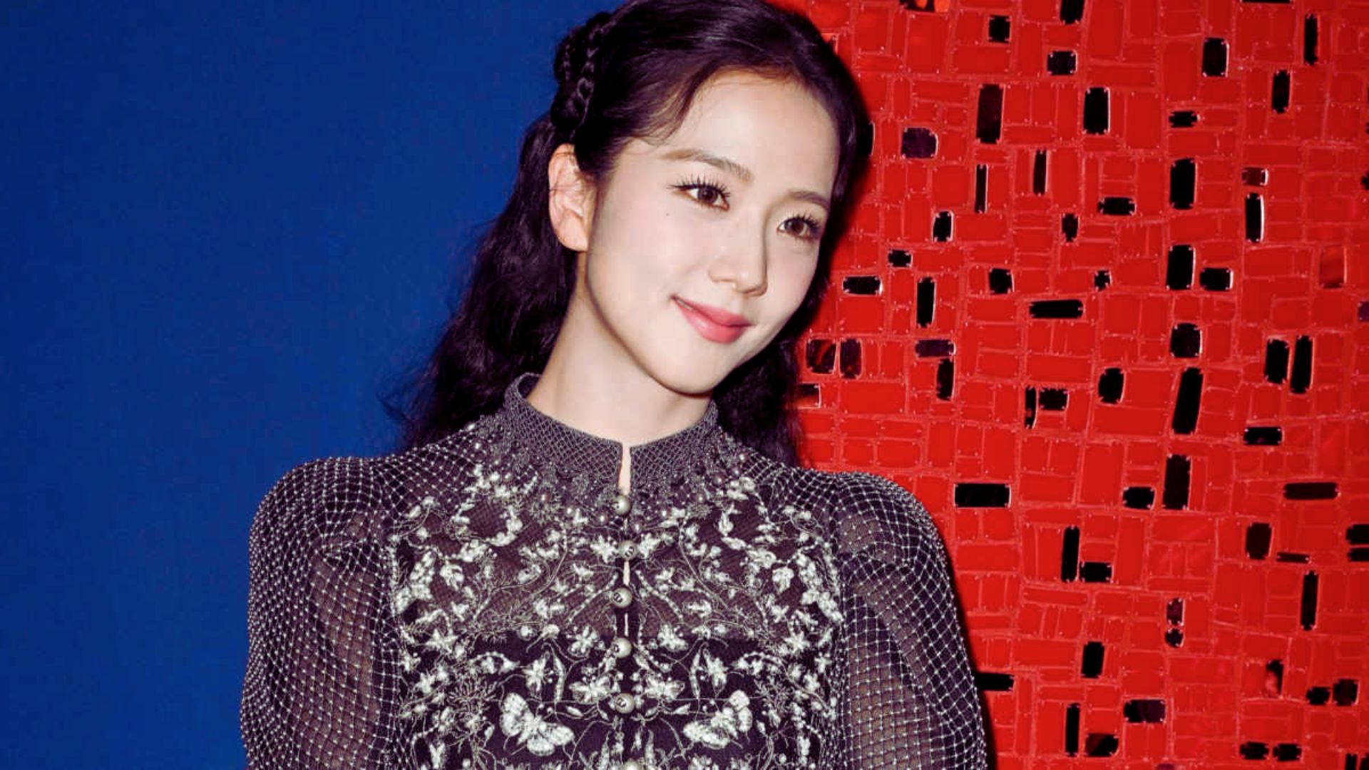 2. A woman wearing a black dress poses against a striking red wall.