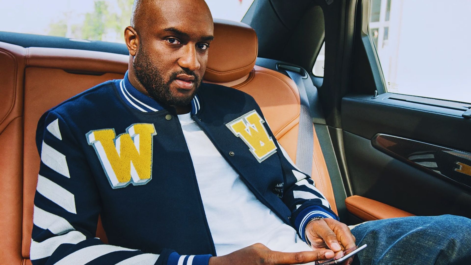 A man sitting in the back seat of a car, focused on his phone, with a thoughtful expression on his face.
