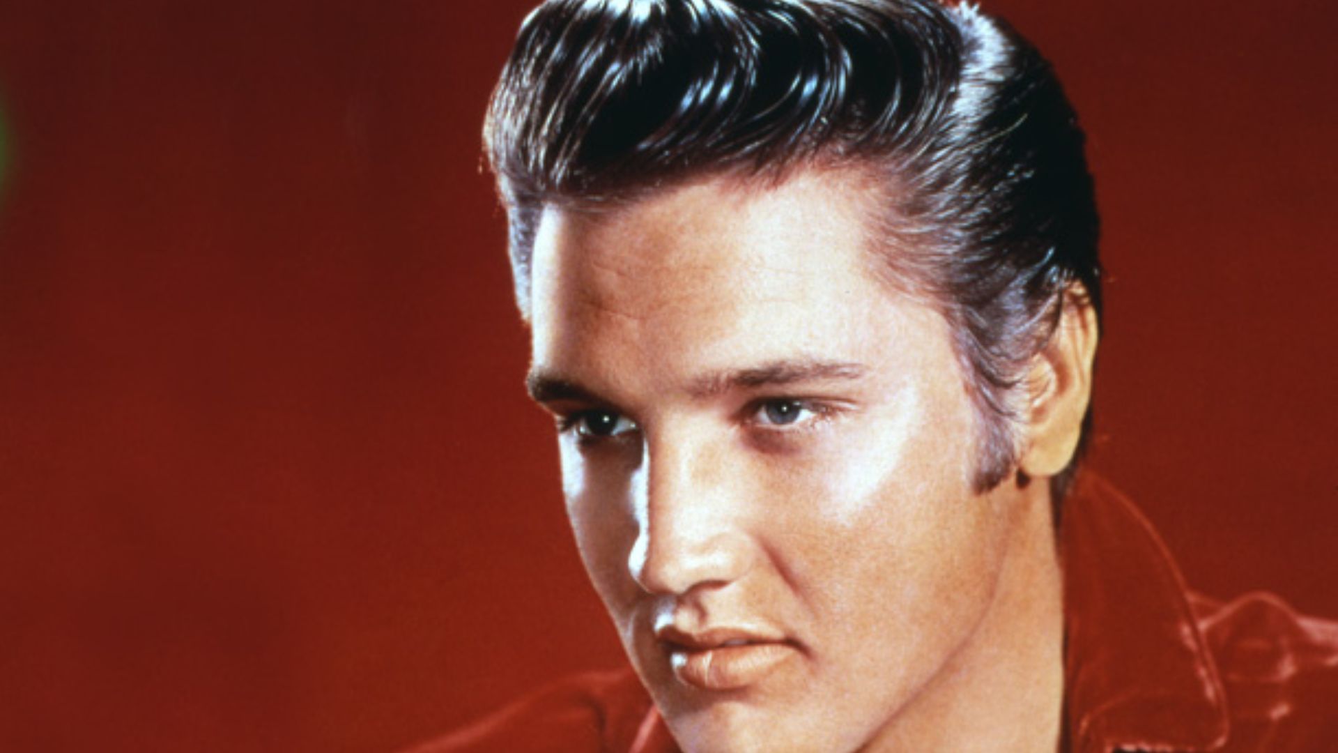 Elvis Presley wearing a red shirt, showcasing his iconic black hair and charismatic presence.