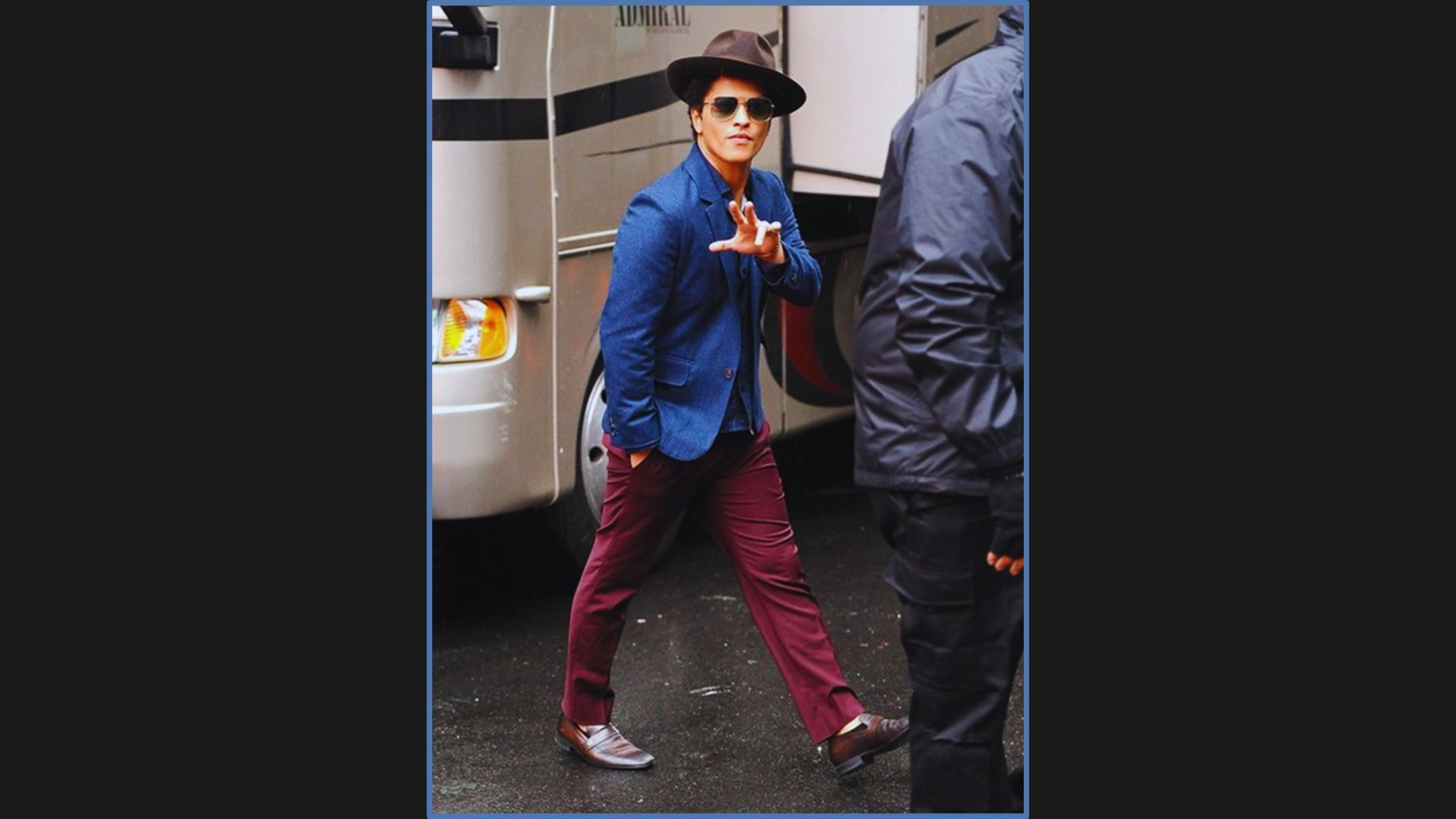 Bruno Mars in hat, a blue blazer, and brown boots, probably waving to the media.