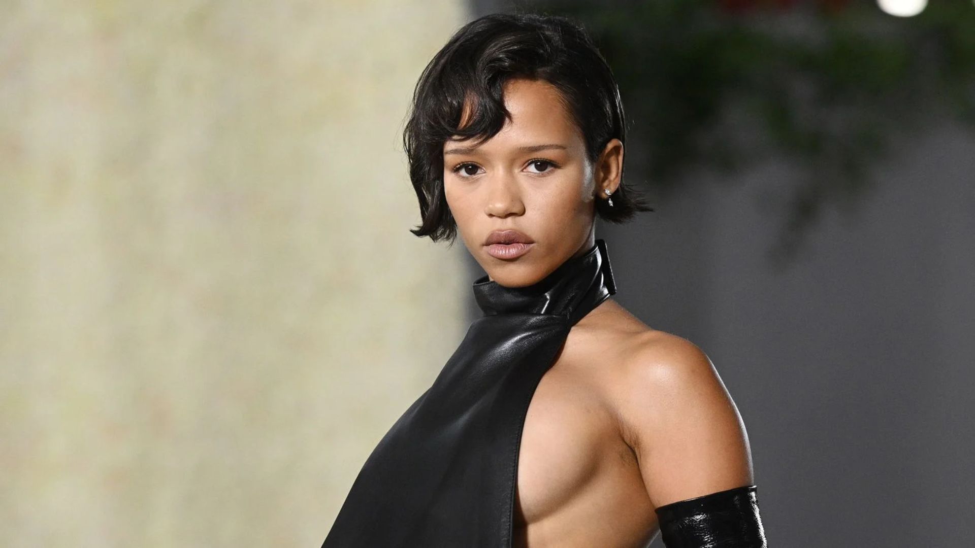A woman wearing a stylish leather dress and matching gloves, posing confidently against a neutral background.