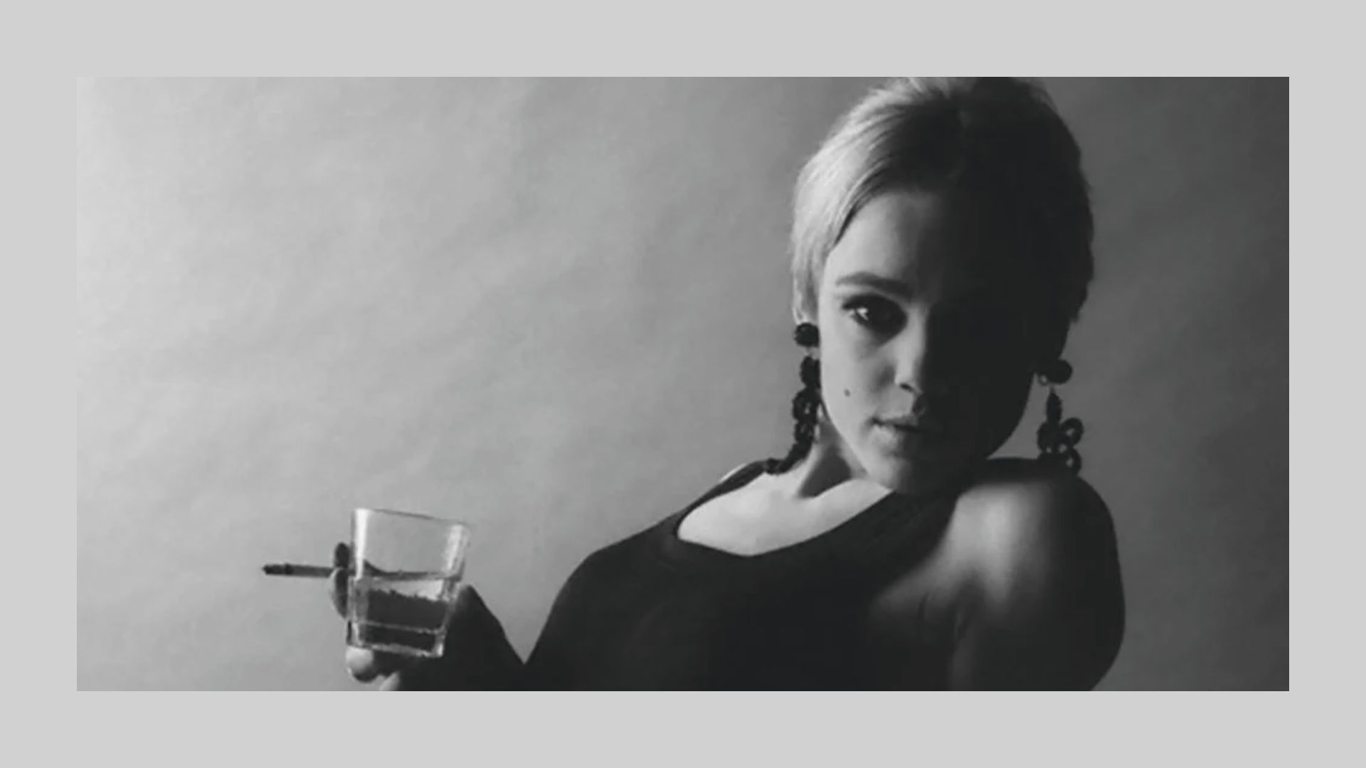 A woman holding a glass in one hand and a cigarette in the other, looking contemplative.