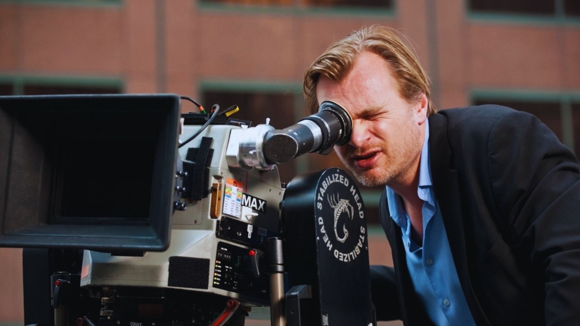 A man in a suit peers through a camera lens, embodying the creative vision of filmmaker Christopher Nolan.