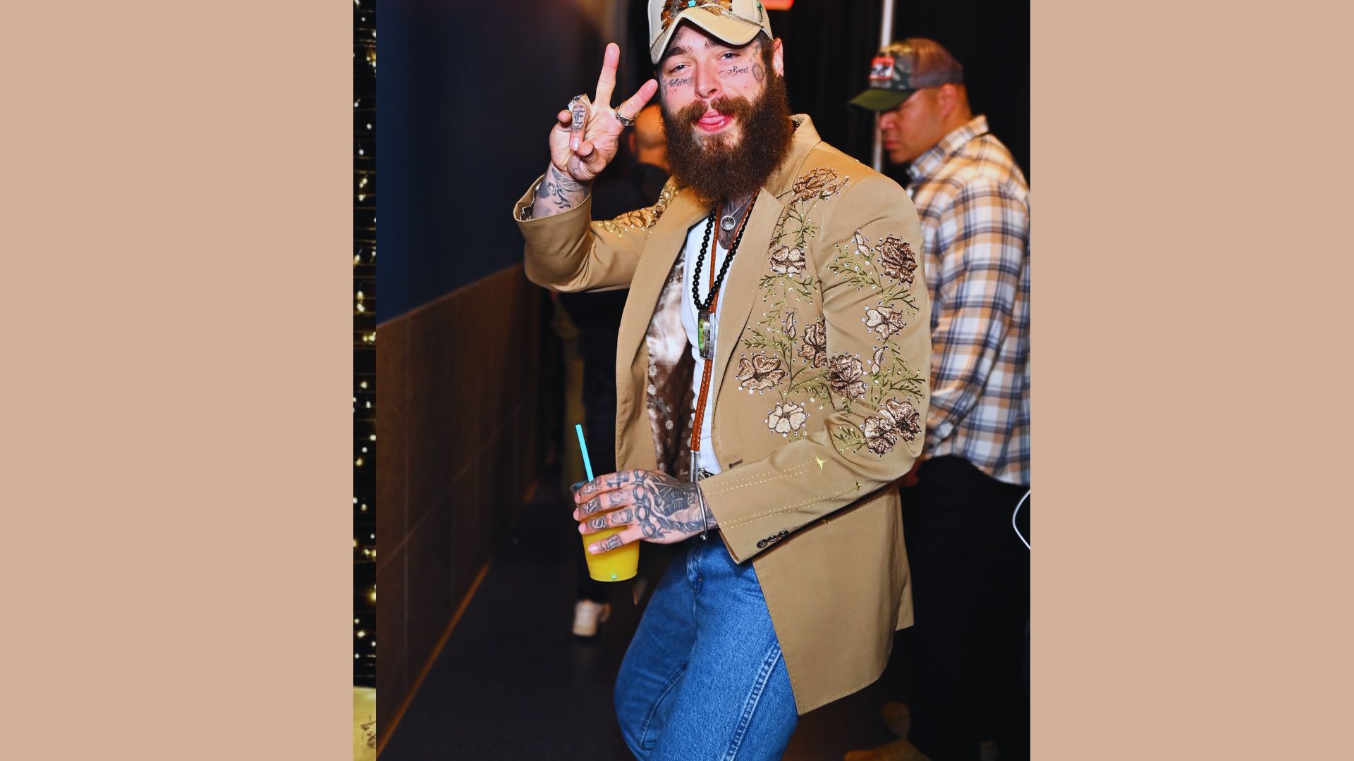 A bearded man wearing a hat holds a drink, smiling as he enjoys his beverage.