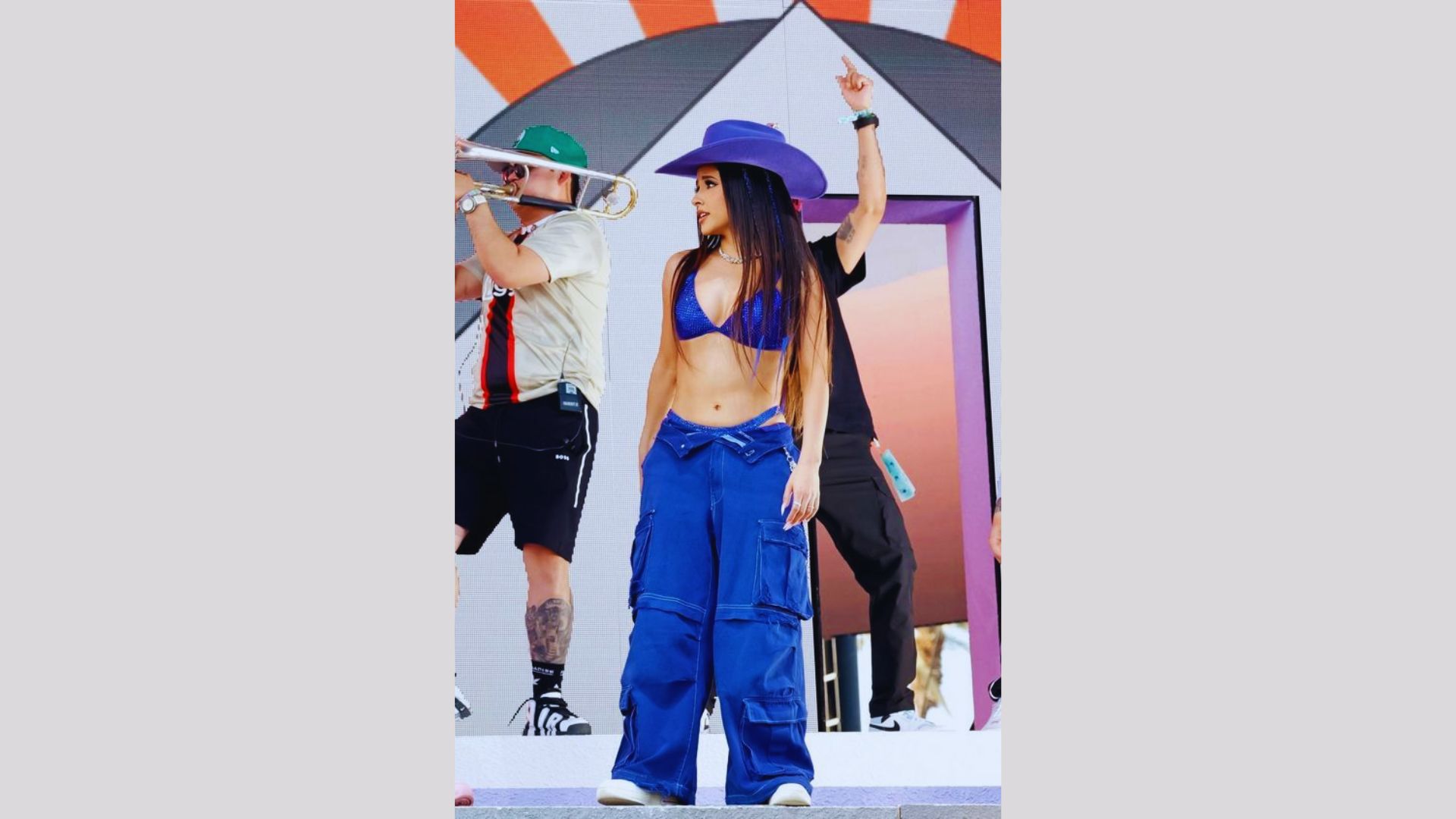 A woman wearing blue pants and a hat stands confidently, showcasing her casual style.