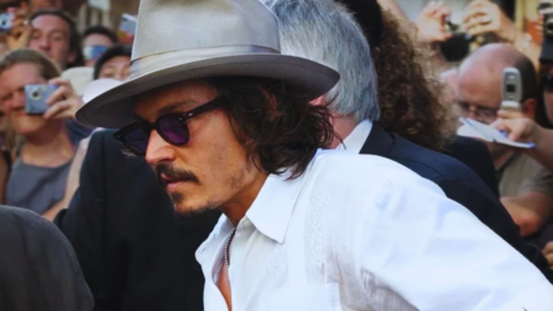 2. Johnny Depp at a movie premiere, sporting a hat and sunglasses, smiling for the cameras.
