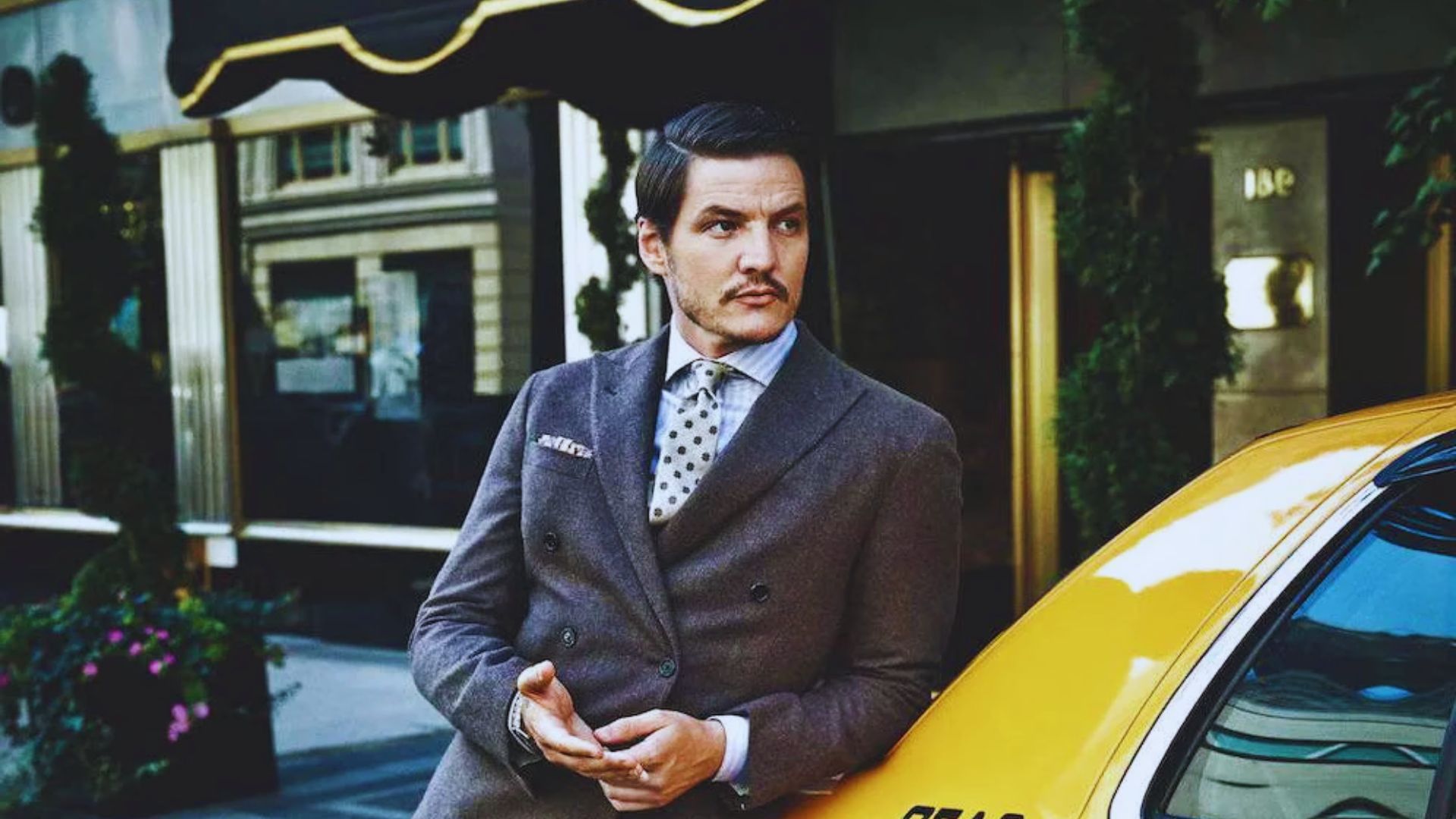 A man in a suit and tie leans against a yellow taxi, exuding a professional and relaxed demeanor.