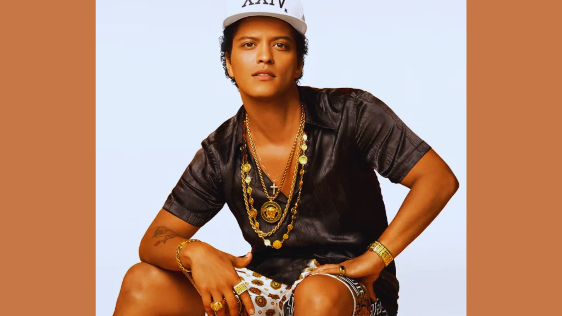 Bruno Mars in a cool outfit with a cap and stylish gold accessories.