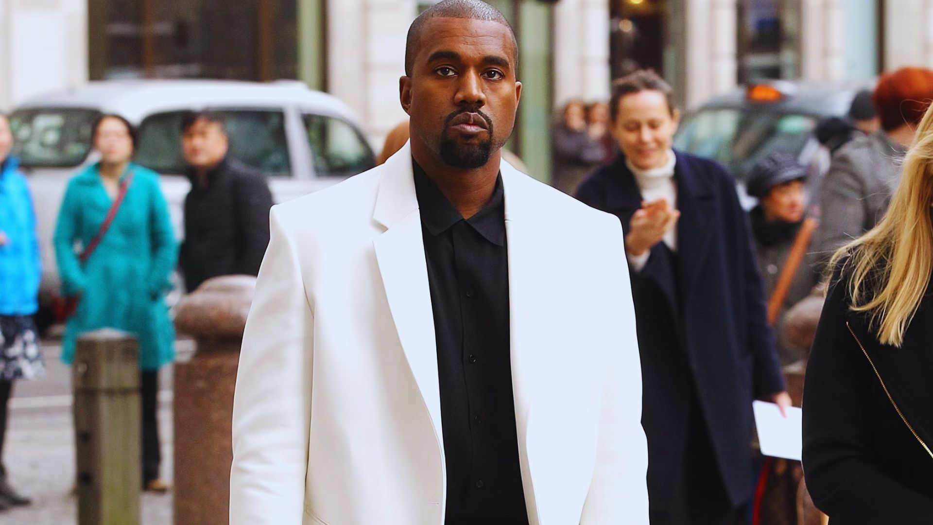 Kanye West wearing a white suit and black shirt, presenting a sharp and fashionable appearance.