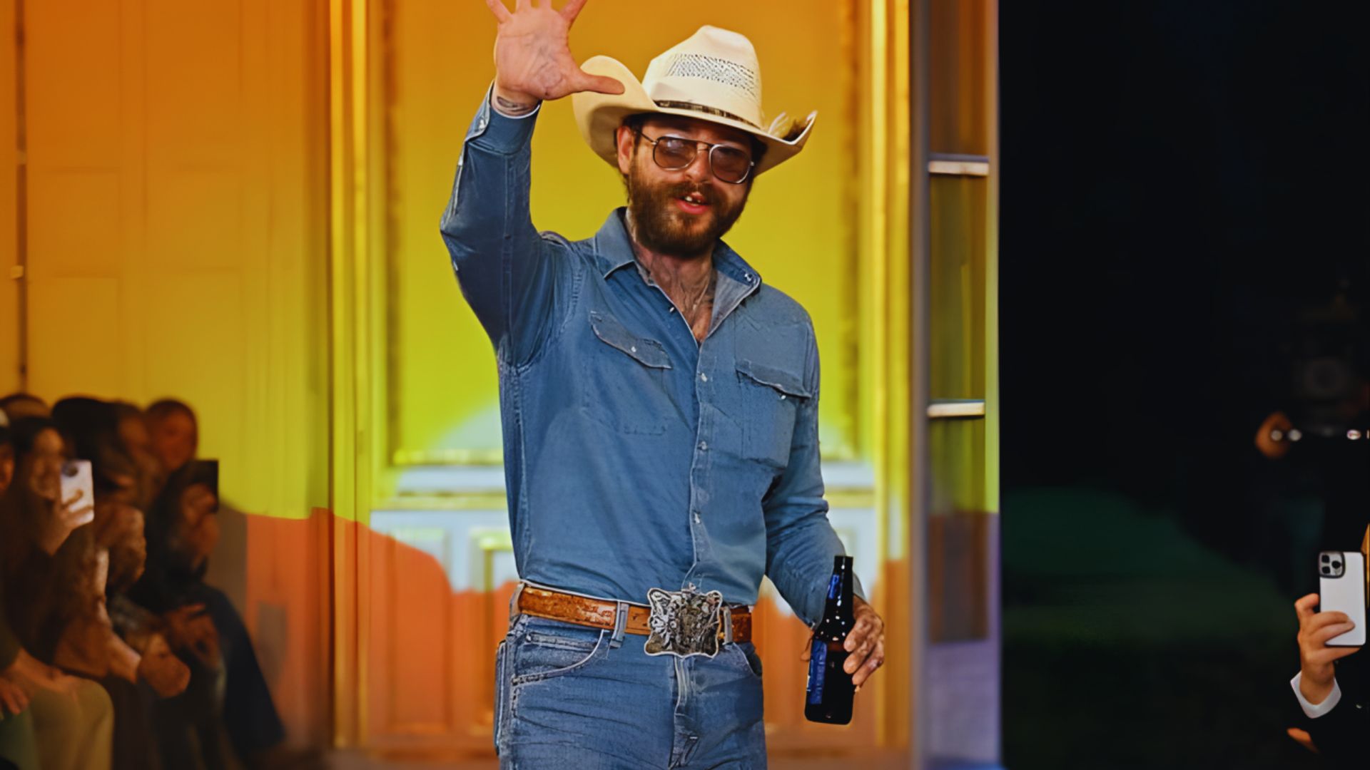 Two men wearing cowboy hats and jeans walk confidently down a runway.