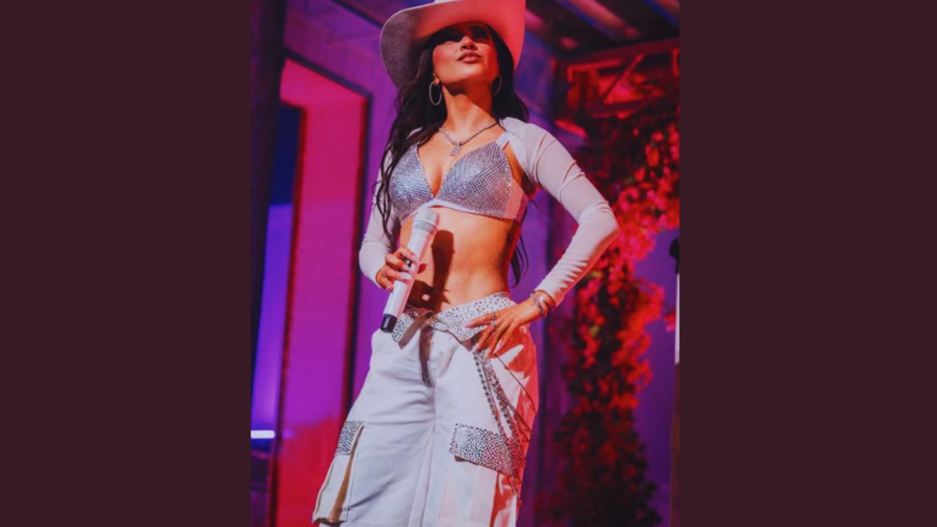 A woman wearing a cowboy hat and white pants stands confidently, showcasing her stylish western-inspired outfit.