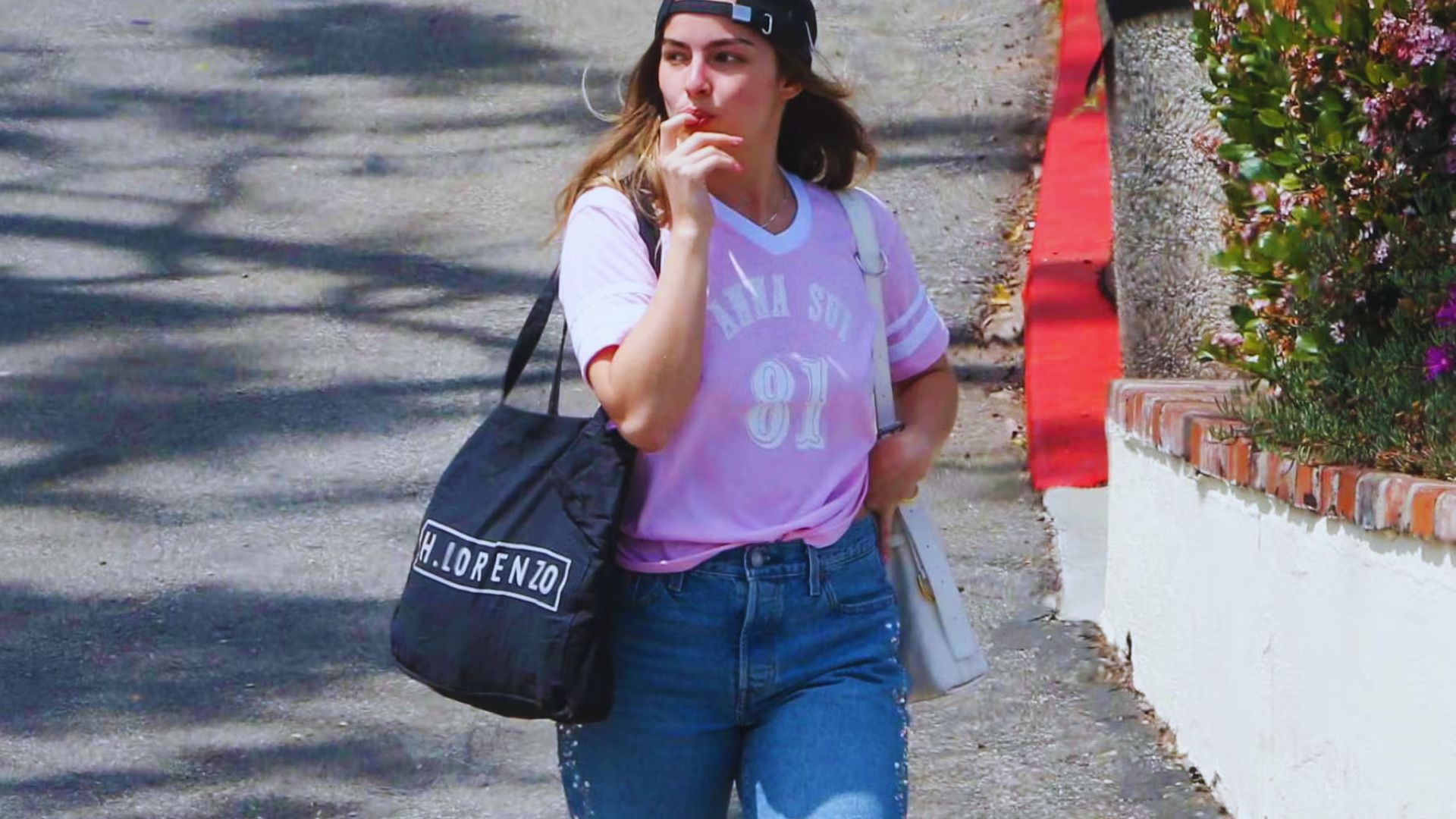 A woman in a pink shirt and jeans walks down the street, surrounded by urban scenery.