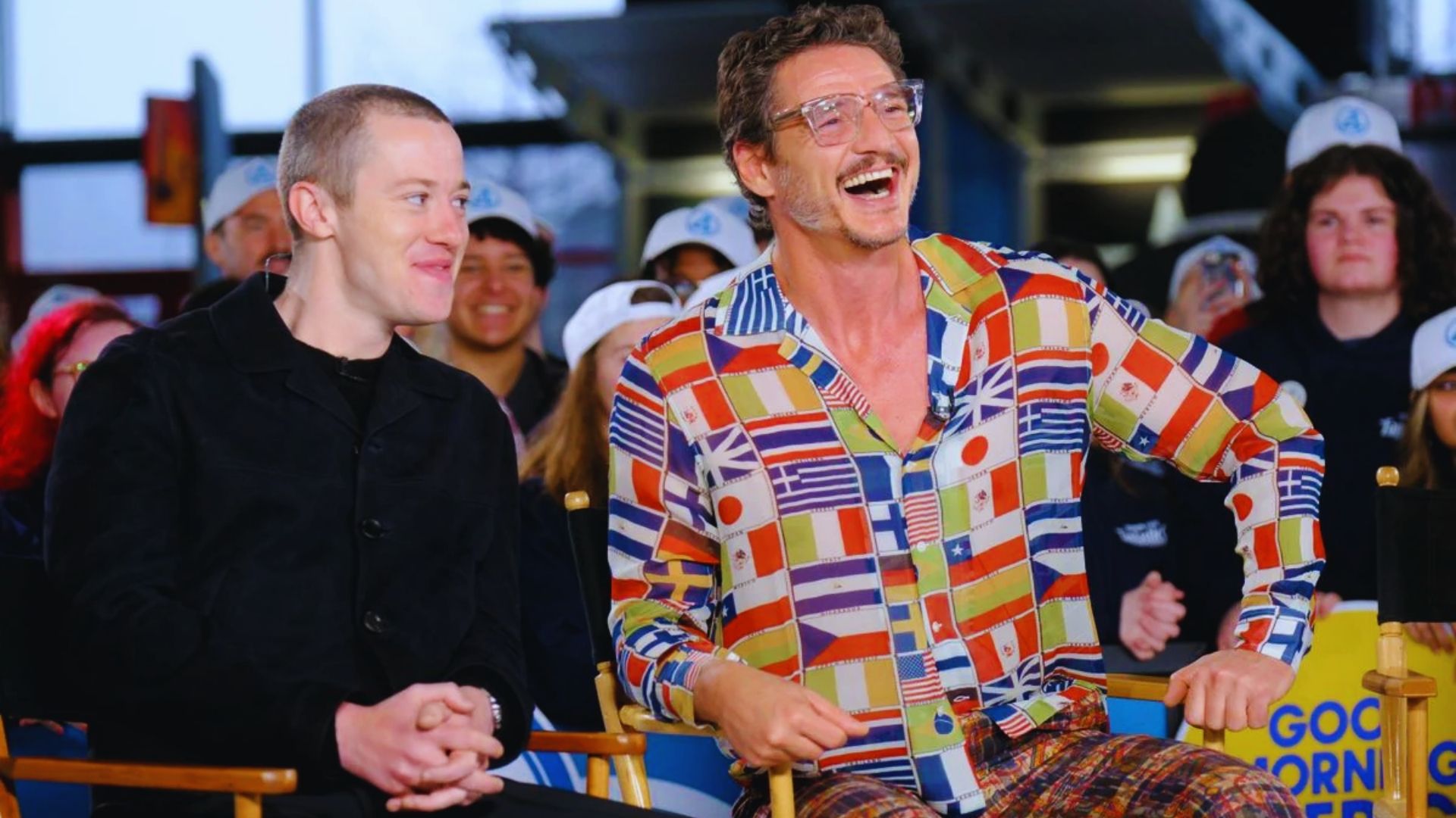 1. Two men sitting in chairs, laughing and smiling together in a relaxed setting.