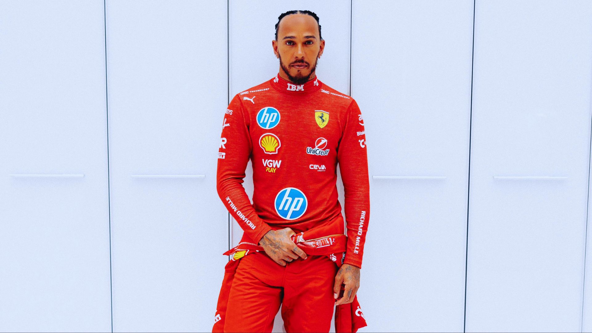 A man in a red suit stands beside a textured wall, exuding confidence and style.