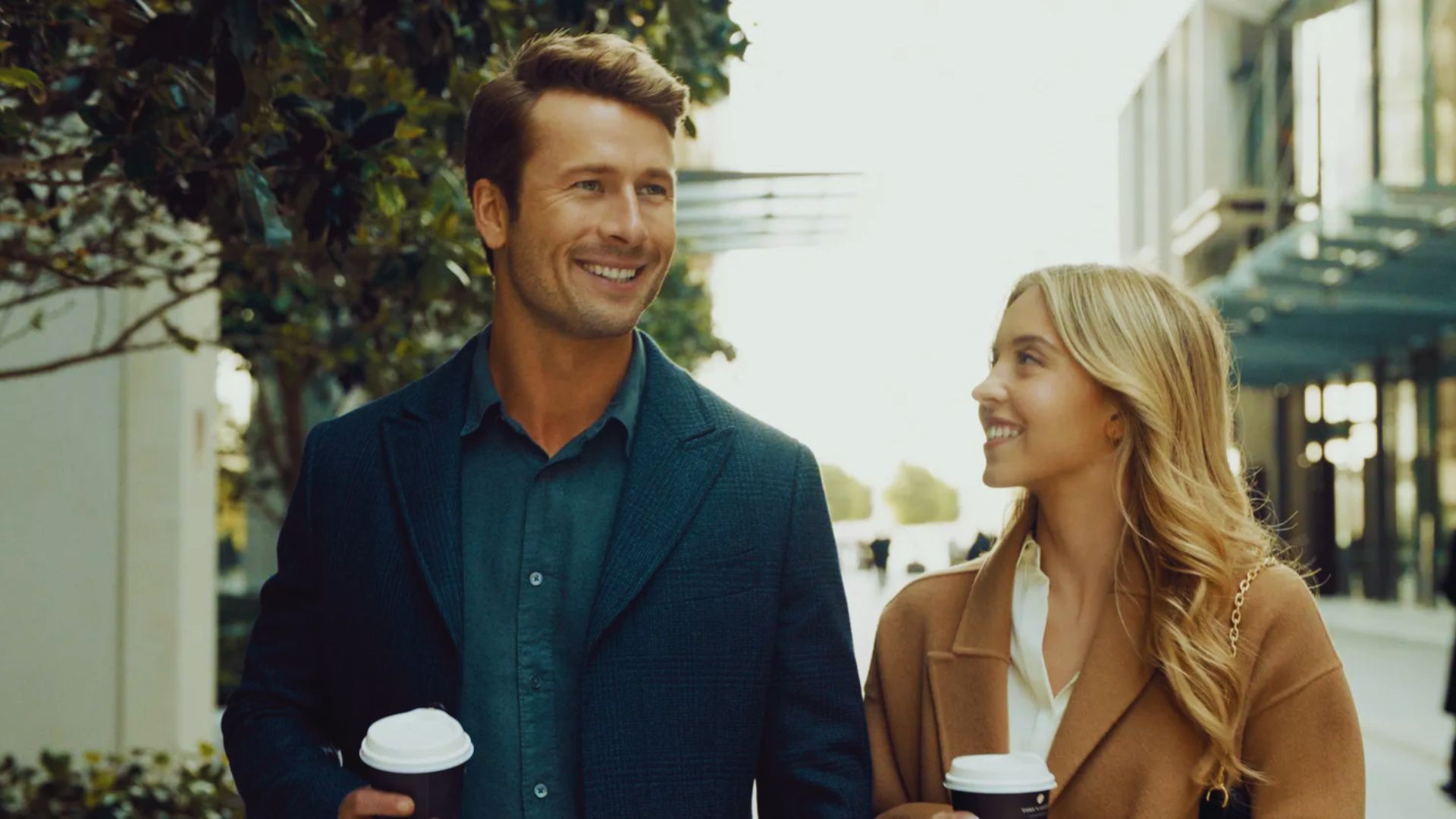 Glen Powell with a woman, having a good conversation outside a coffee shop.
