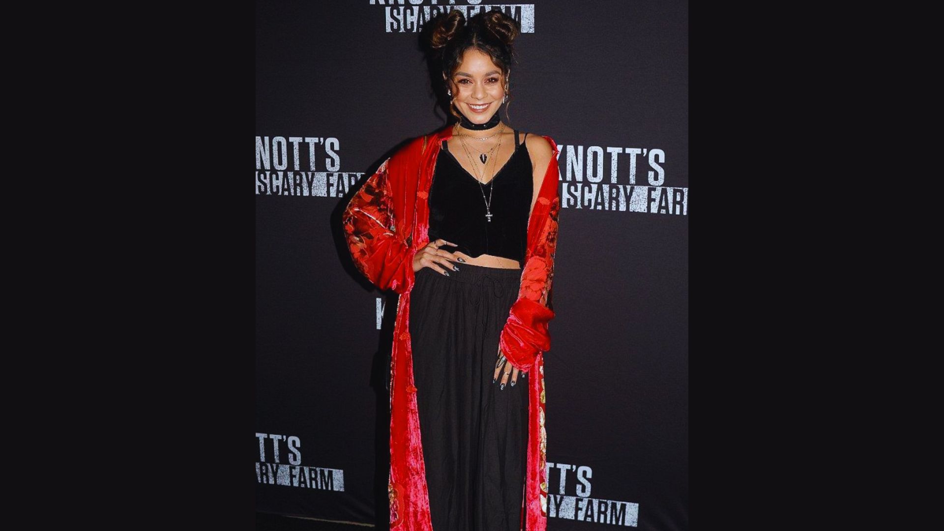 A woman wearing a red dress with a black top stands on the red carpet, striking a pose for the cameras.