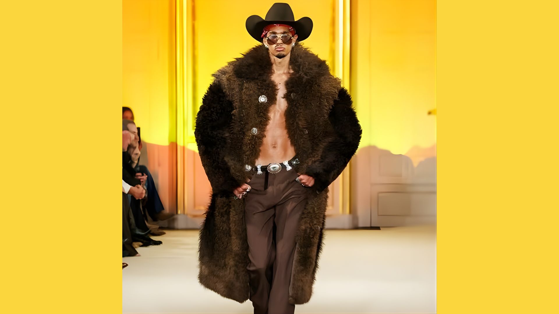 . A man wearing a fur coat and hat confidently walks down the runway, showcasing a bold fashion statement.