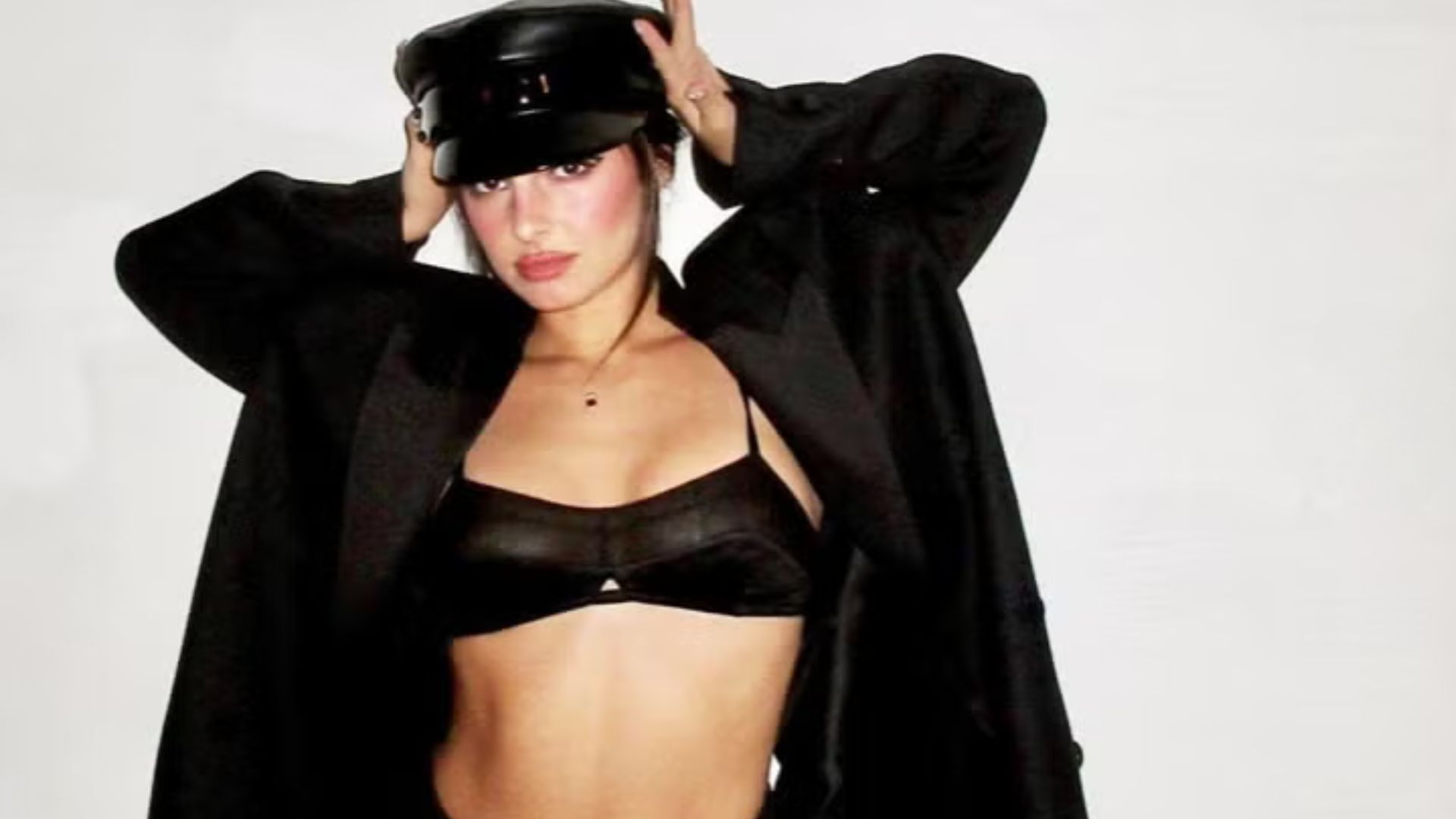 A woman wearing a black bra top under a stylish jacket, posing confidently against a neutral background.