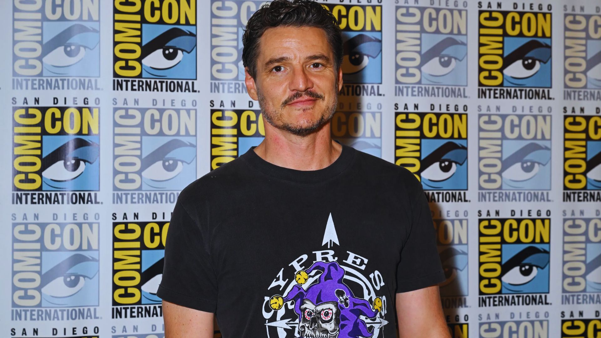 A man in a black shirt with a purple shirt underneath, displaying a trendy and casual ensemble.