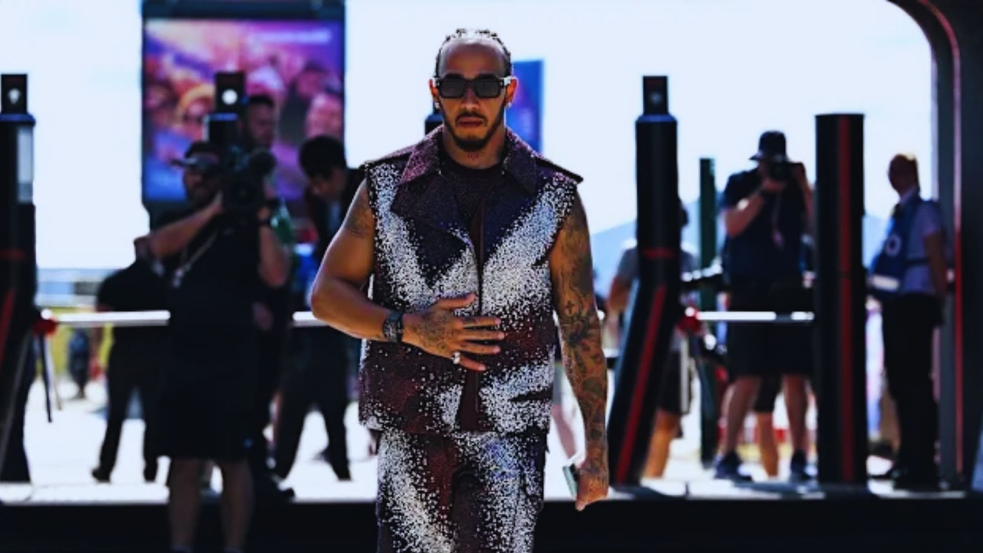 A well-dressed man in a suit and sunglasses strides down a runway, exuding confidence and elegance.